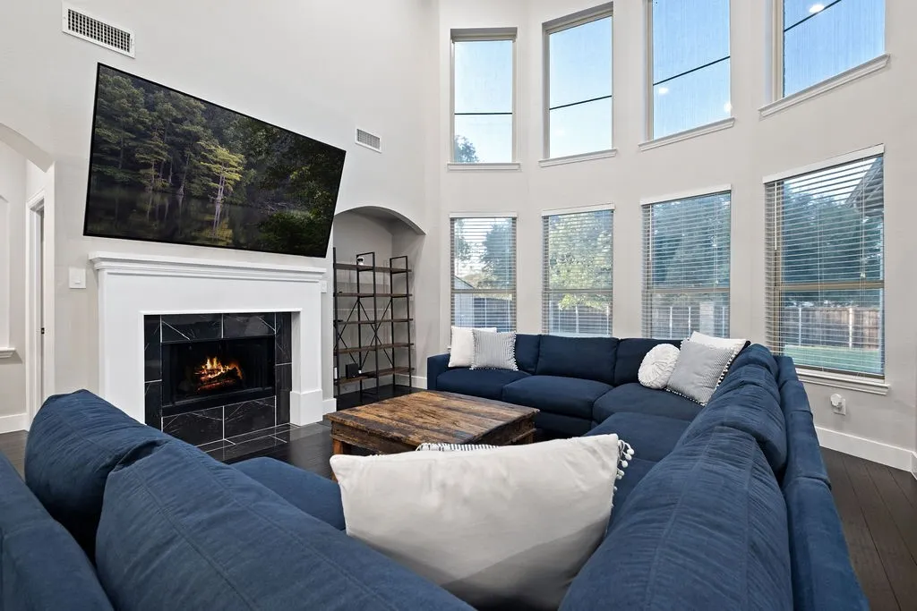 Spacious living area featuring a fireplace with black tile surround, white mantel, and wood-finish flooring