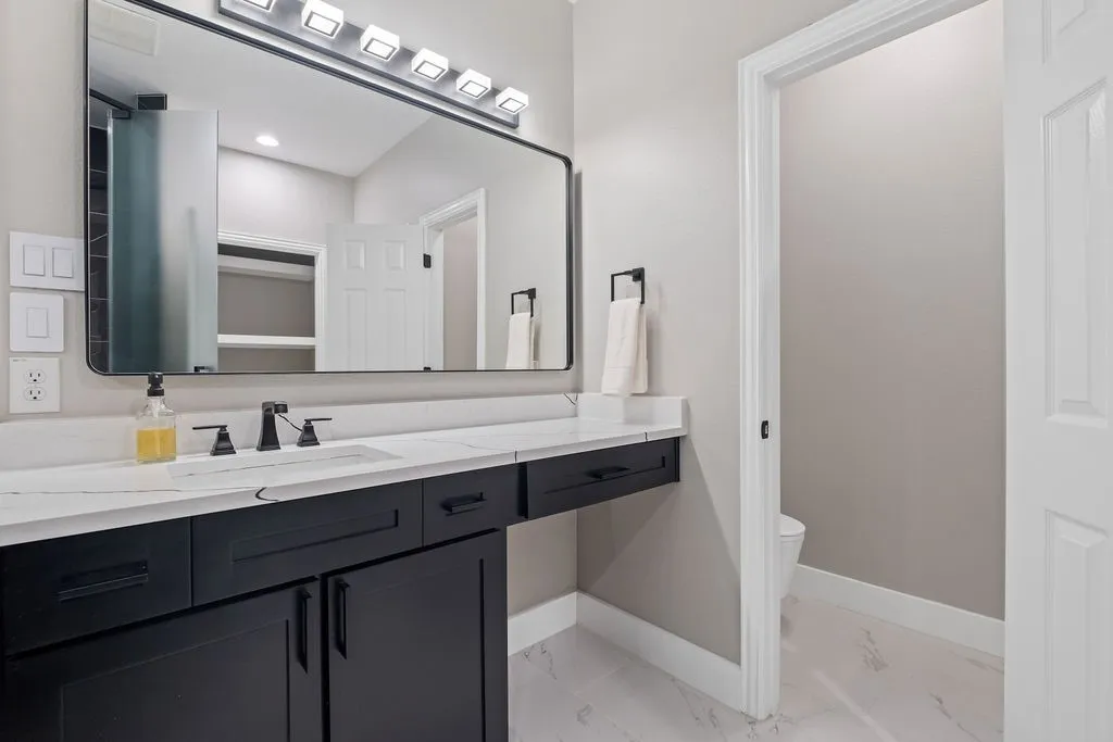 Black framed rectangular mirror, black matte vanity light fixture, elongated rectangular under-mount sink, black finish widespread faucet, and black cabinetry with integrated pulls