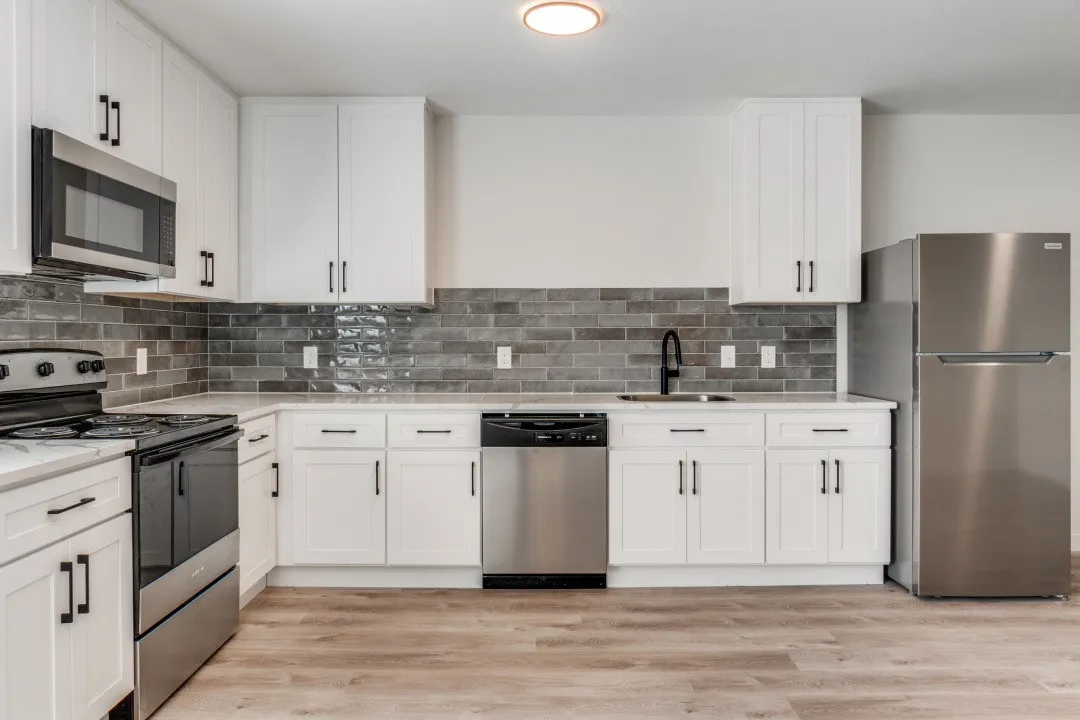 Kitchen featuring white cabinetry, stainless steel appliances, dark subway tile backsplash, light countertops, and wood-finish flooring