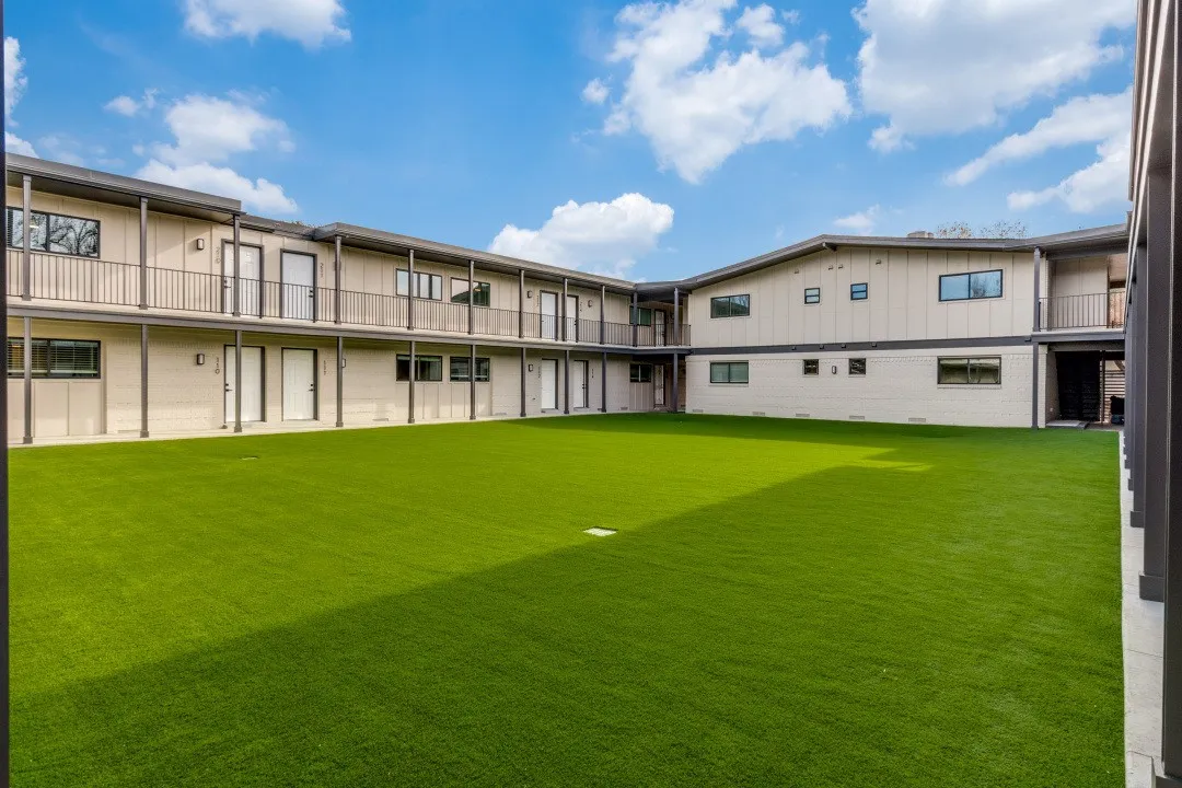 Expansive artificial turf courtyard surrounded by a multi-story building featuring exterior walkways and balconies with dark metal railings