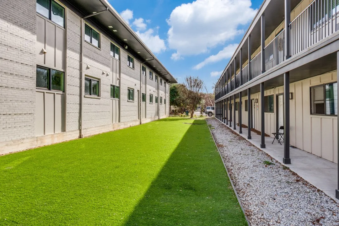 Outdoor space featuring a synthetic turf lawn, gravel pathway, brick facade, and multi-level balconies with metal railings