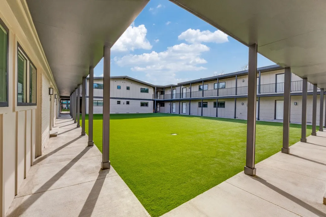 Central courtyard with artificial turf, surrounded by two-story buildings featuring balconies, covered walkways, and modern exterior lighting
