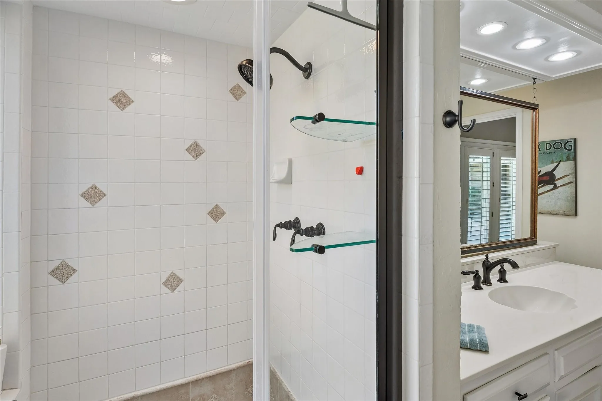 White tiled shower with decorative accent tiles, framed glass shower enclosure, and dark bronze fixtures