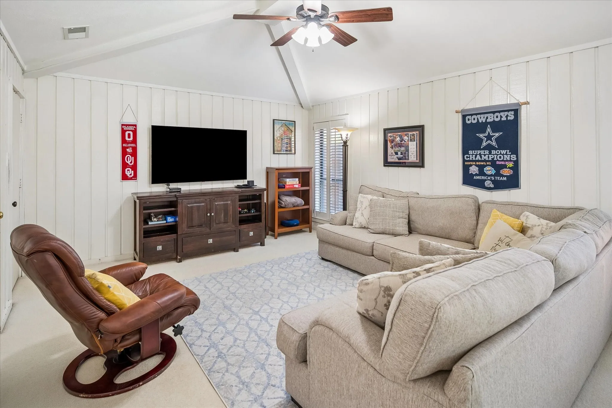 Vaulted ceiling with exposed beams, wood-tone ceiling fan, and painted vertical paneling
