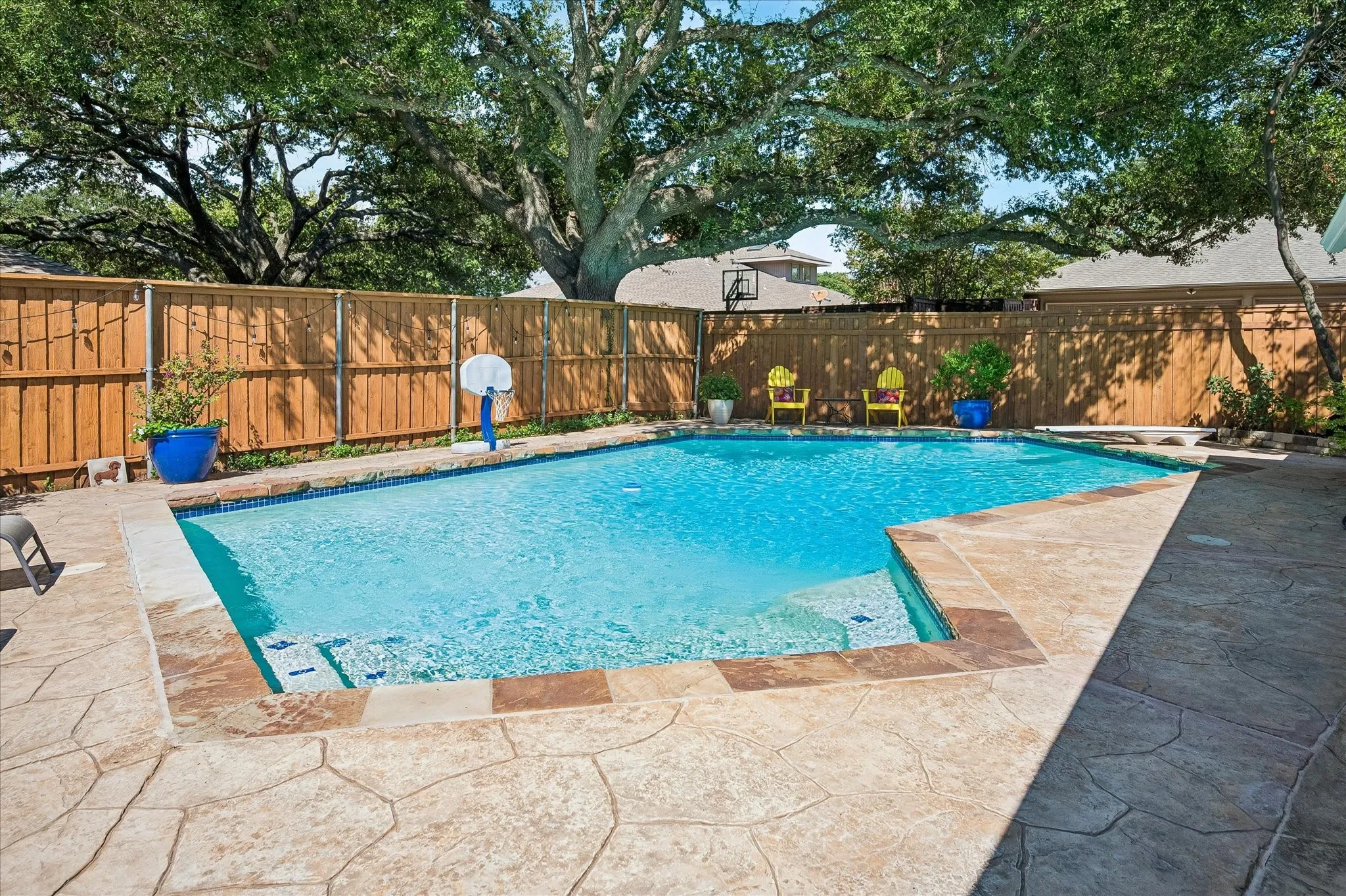 Swimming pool with integrated steps, surrounded by stamped concrete decking and a wood privacy fence