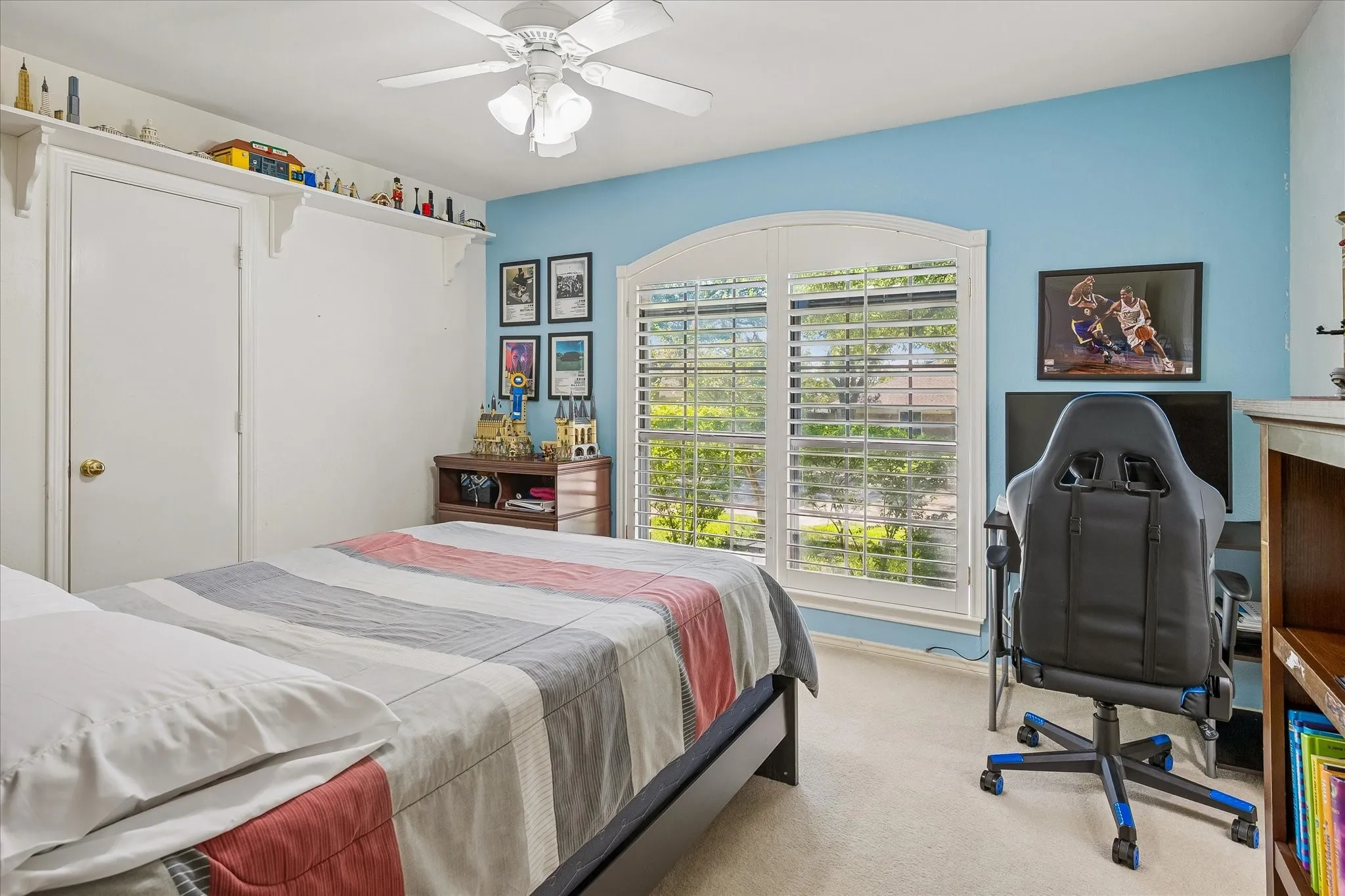 Arched window with plantation shutters, ceiling fan, built-in shelving, and light blue accent wall