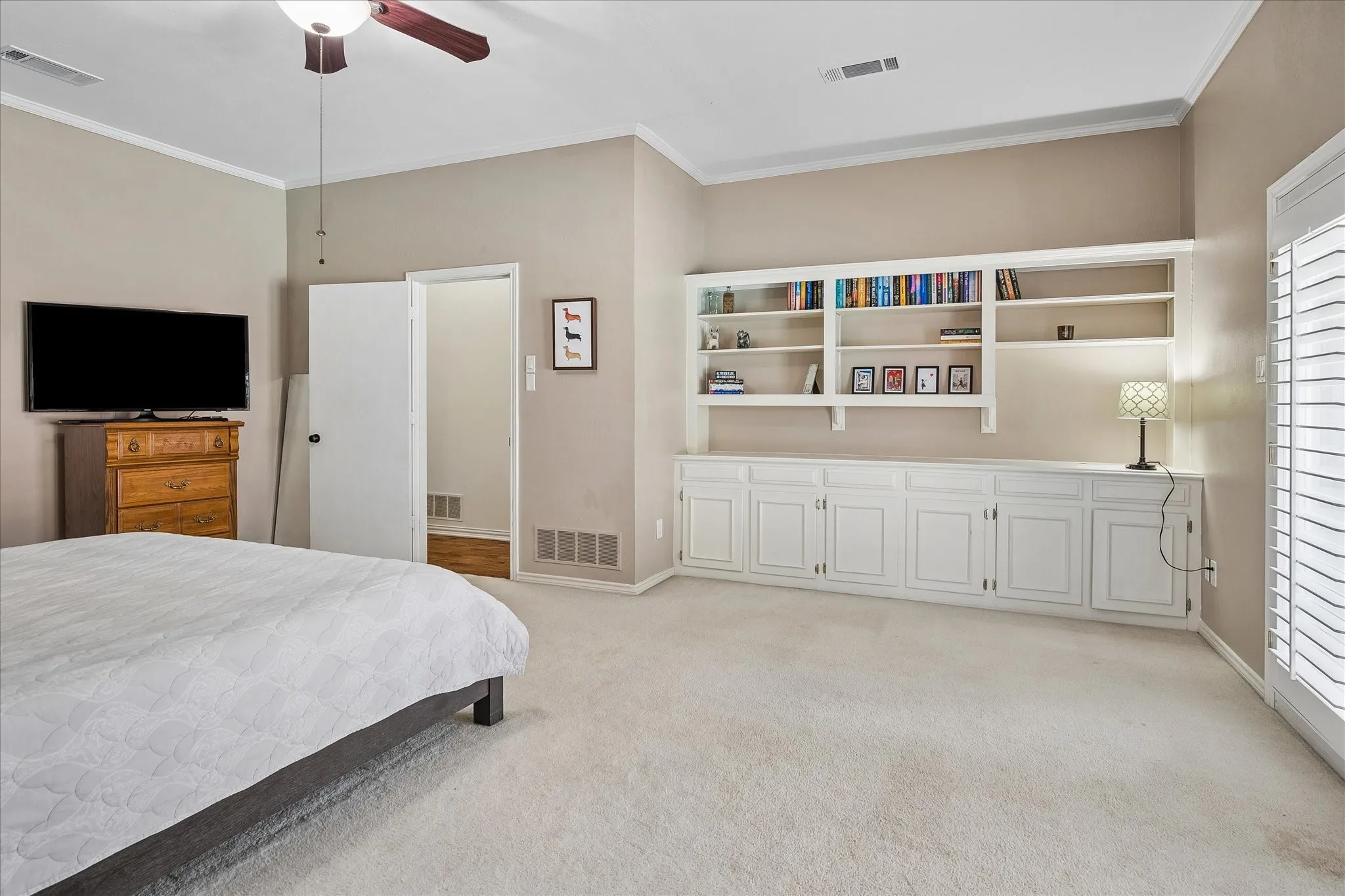 Built-in cabinetry with open shelving, ceiling fan, crown molding, and plantation shutters