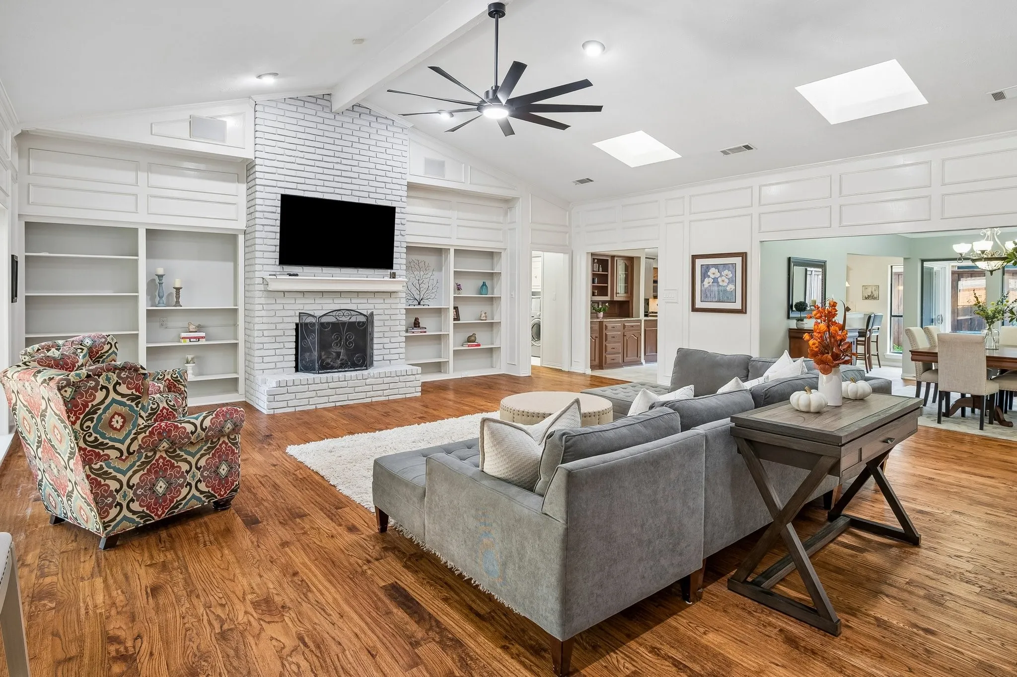 Vaulted ceiling, wood-finish flooring, white brick fireplace, built-in shelving, and skylights