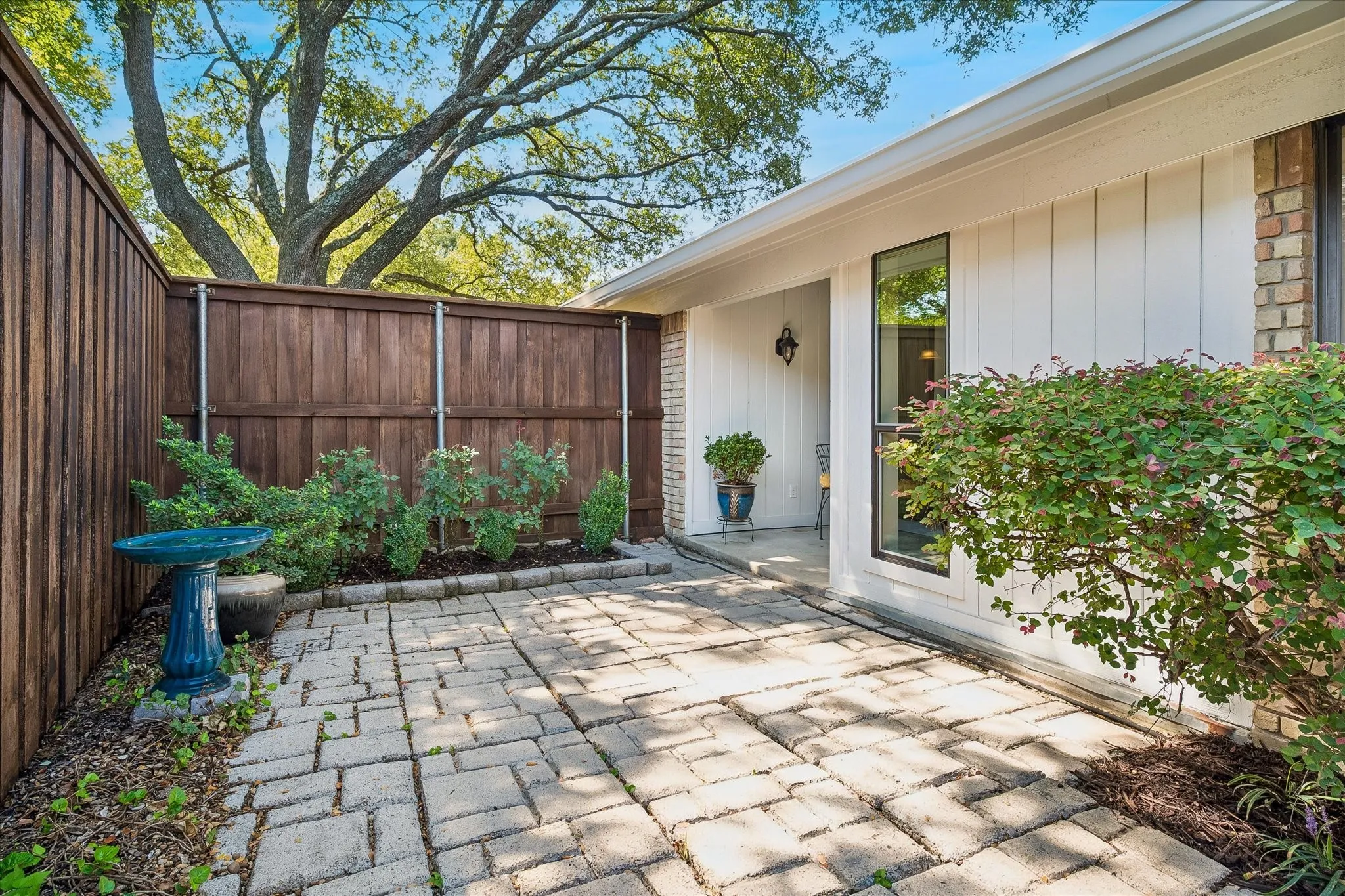 Paved patio with decorative pavers, flanked by a full wood fence and established landscaping
