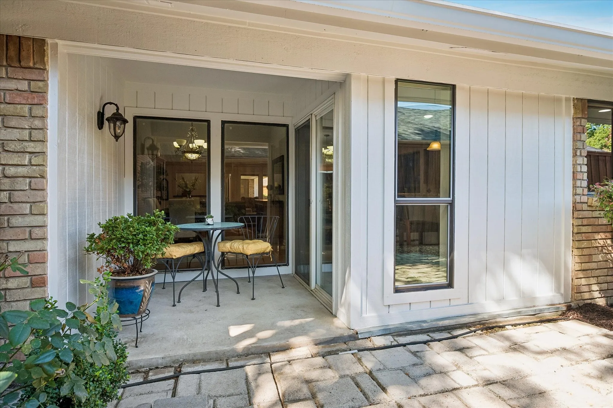 Covered patio with brick and vertical panel siding, featuring a concrete pad and paver walkway