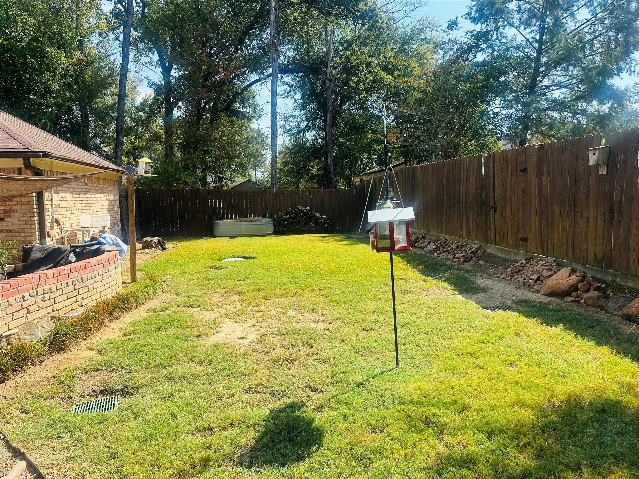 Expansive backyard featuring a wood fence, mature trees, and a brick wall