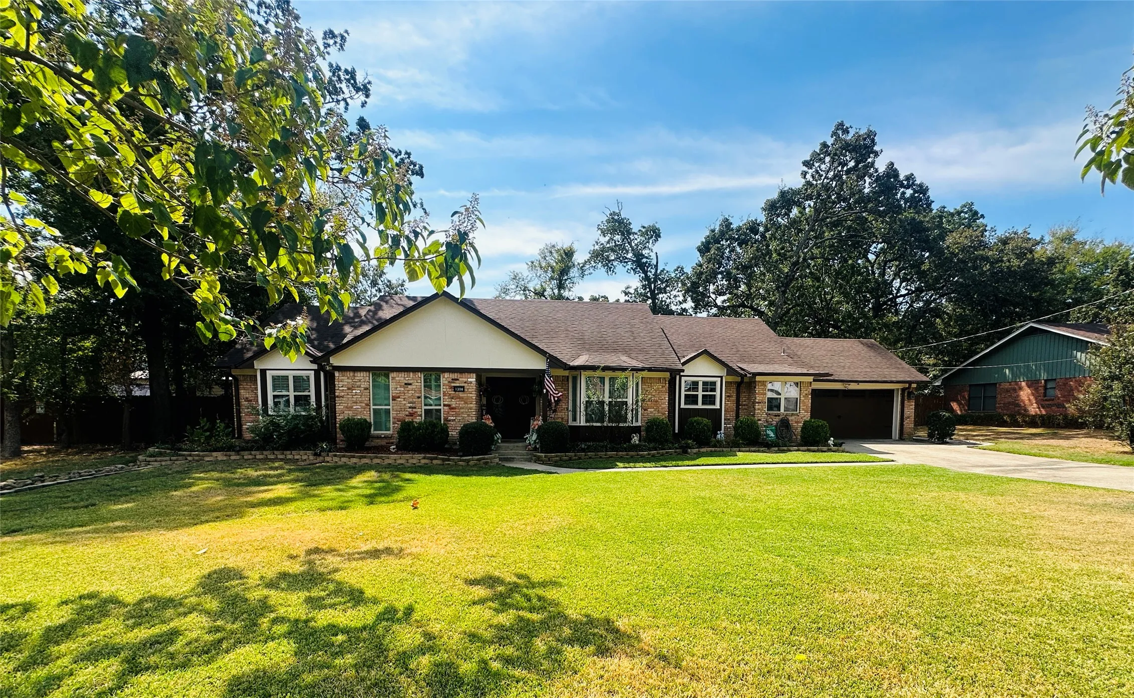 Brick facade with light trim accents, attached garage, front lawn with mature trees, and a concrete driveway