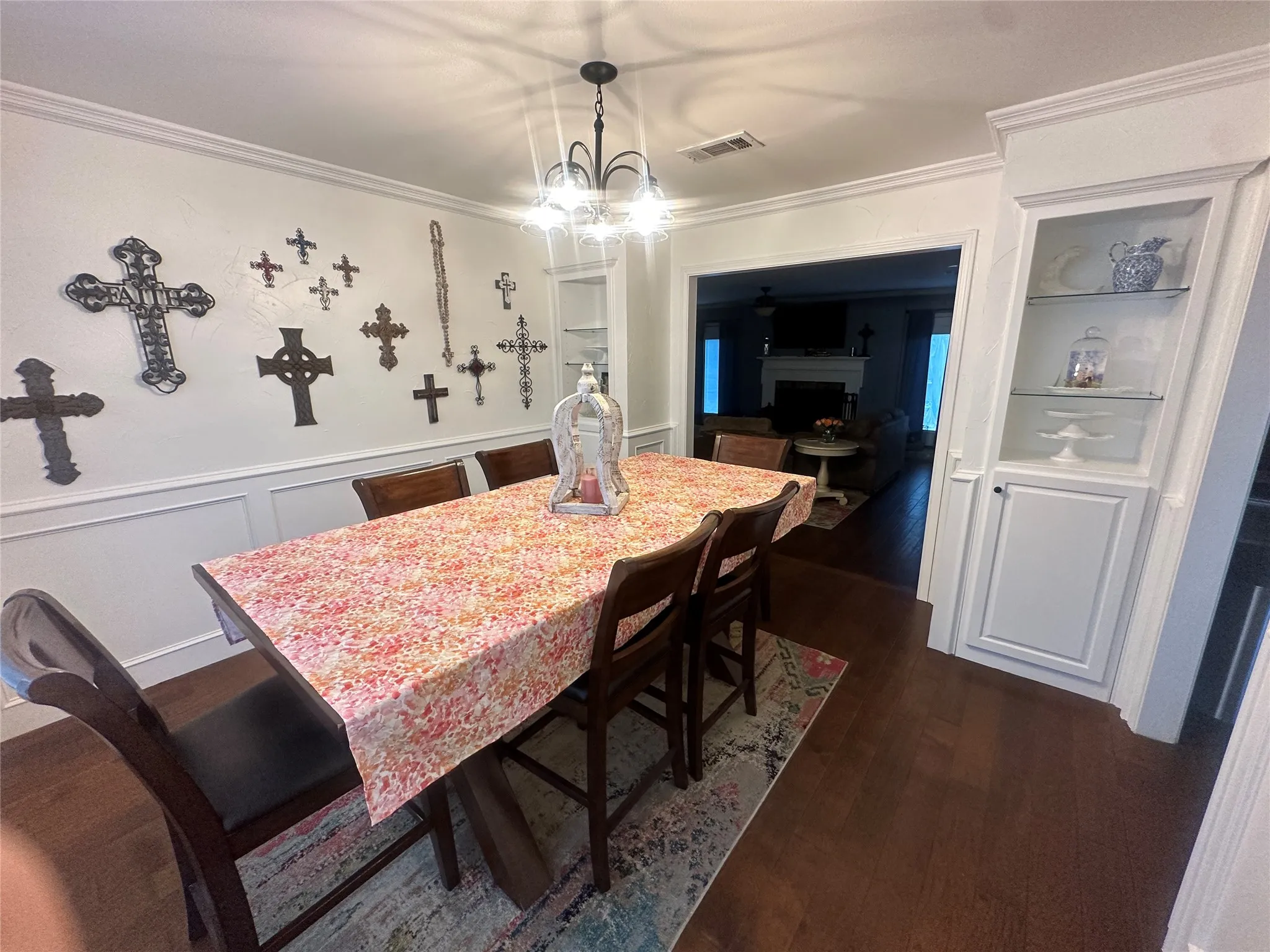 Dark wood-finish flooring, built-in display cabinetry with glass shelving, crown molding, and wainscoting