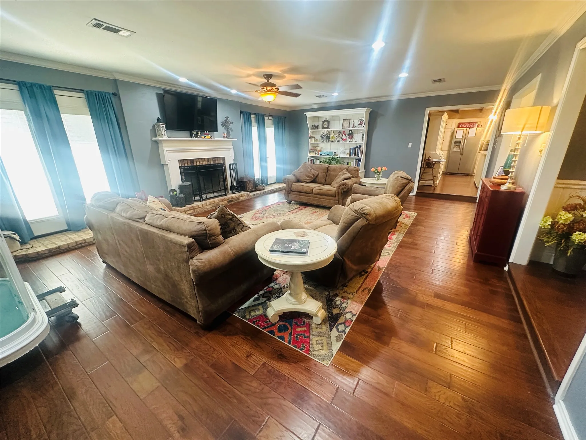 Hardwood flooring throughout, recessed lighting, ceiling fan, and a fireplace with a white mantel and brick hearth