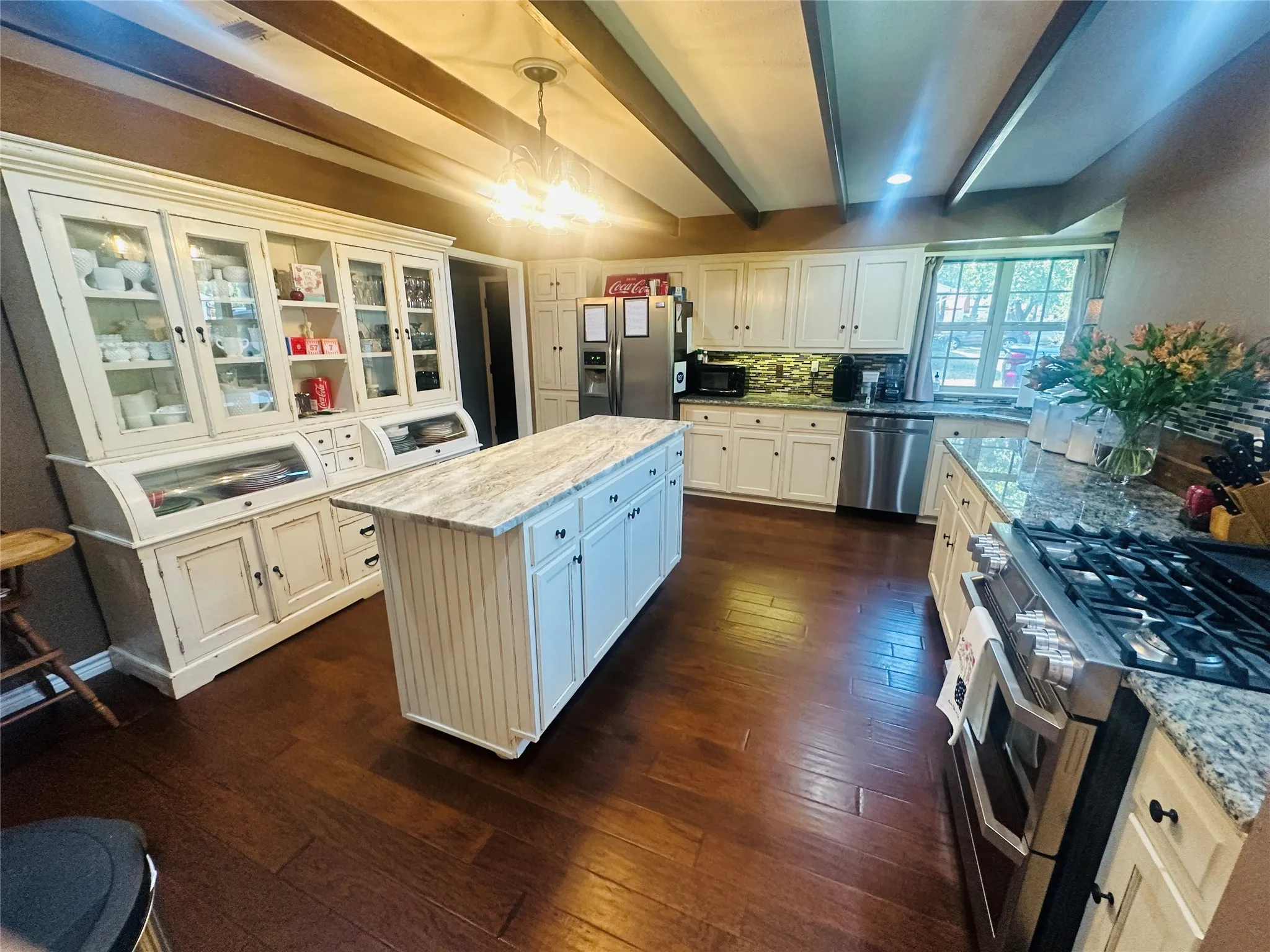 Wood-finish flooring, exposed ceiling beams, white cabinetry, granite countertops, and stainless steel appliances