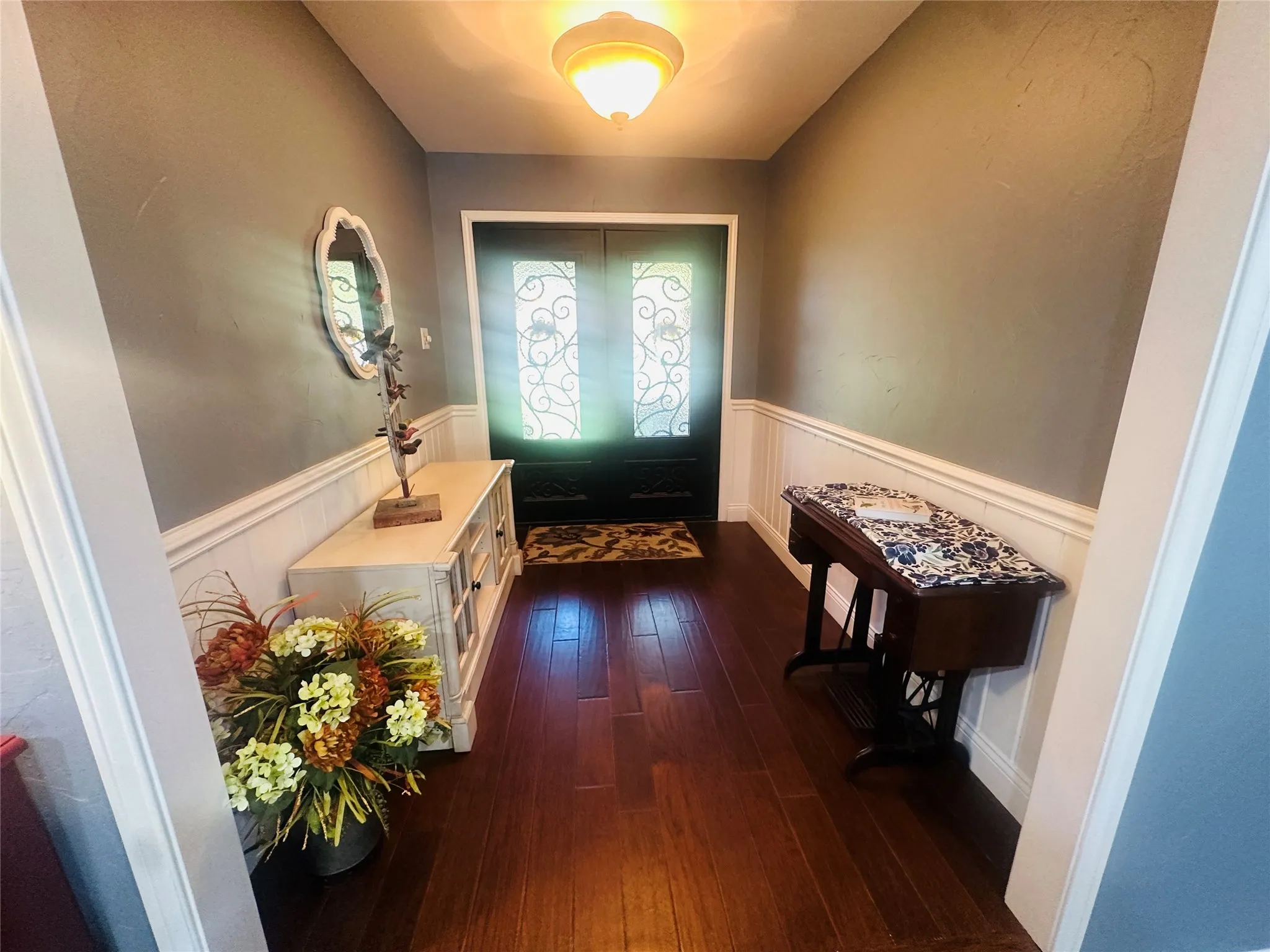 Hardwood flooring, wainscoting, double entry doors with decorative glass inserts, and a semi-flush mount ceiling light fixture