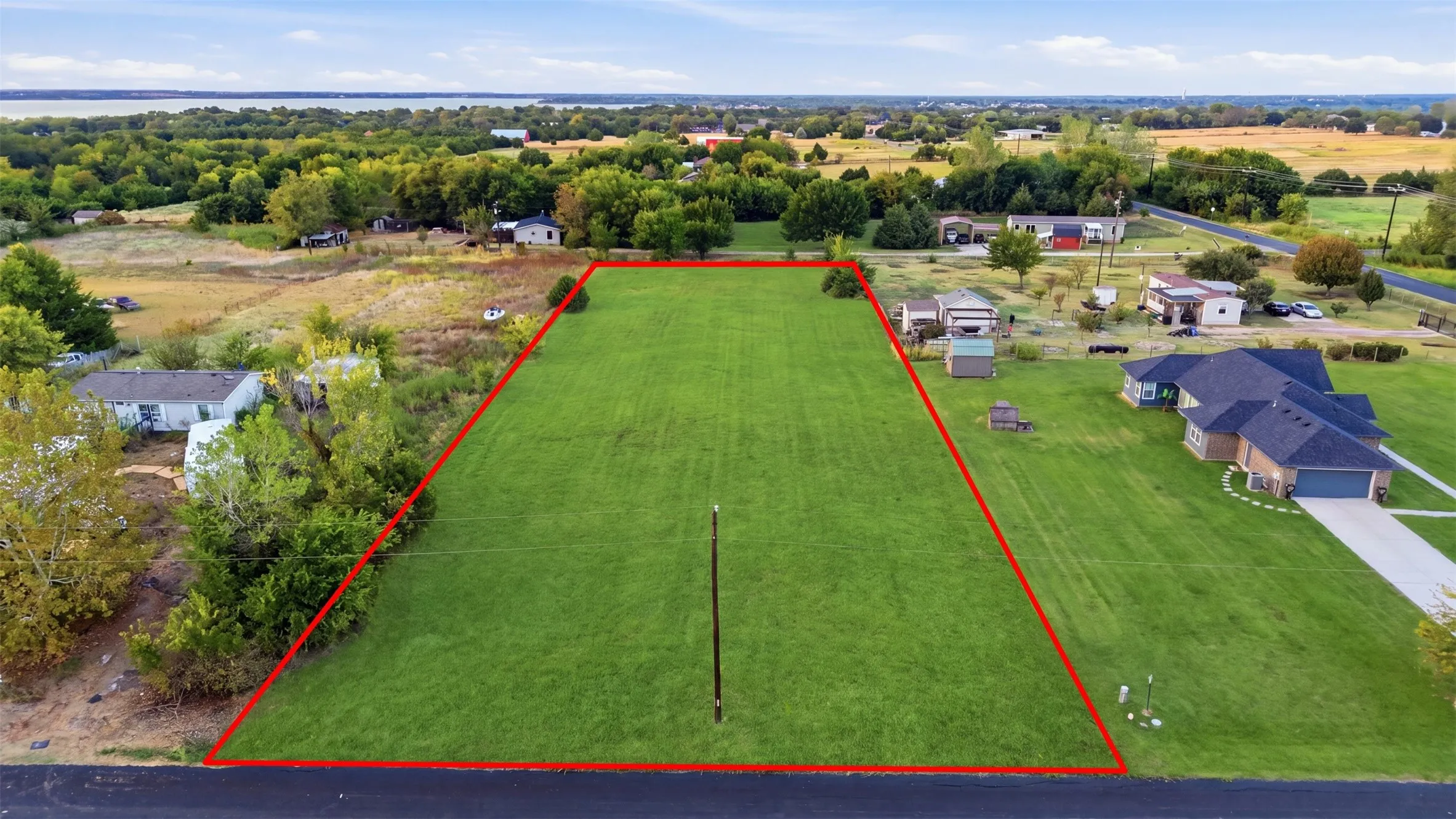 Expansive lot featuring a manicured lawn, established landscaping, and a distant water body
