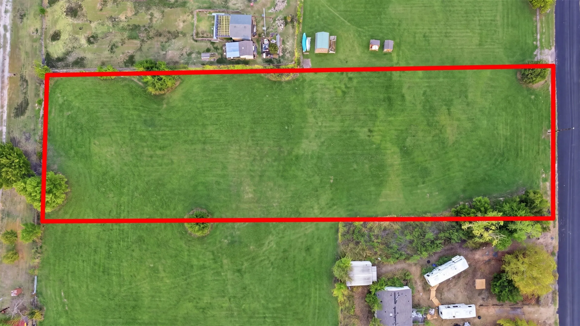 Expansive rectangular lot featuring a verdant grass expanse and scattered mature trees