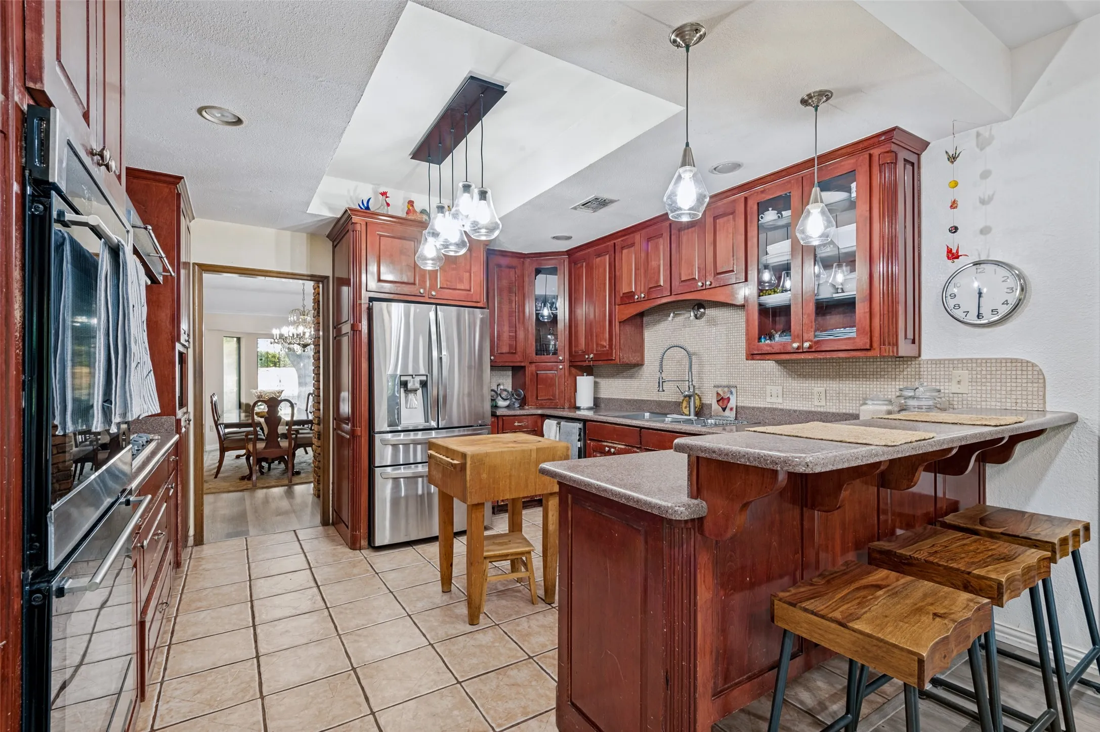 Kitchen featuring wood cabinetry, stainless steel appliances, tile flooring, built-in double ovens, and a breakfast bar
