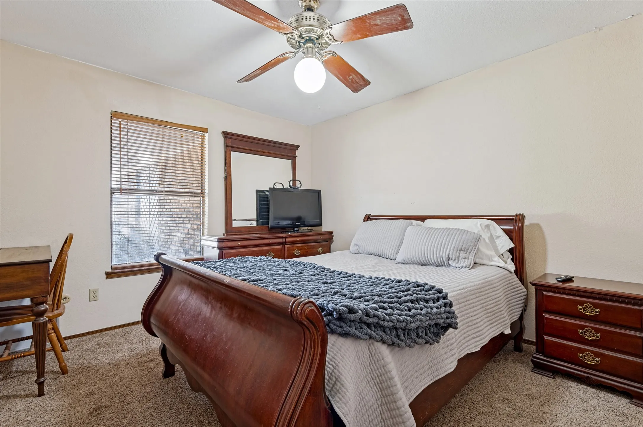 Secondary bedroom with natural light, neutral finishes, window coverings and a ceiling fan with light.