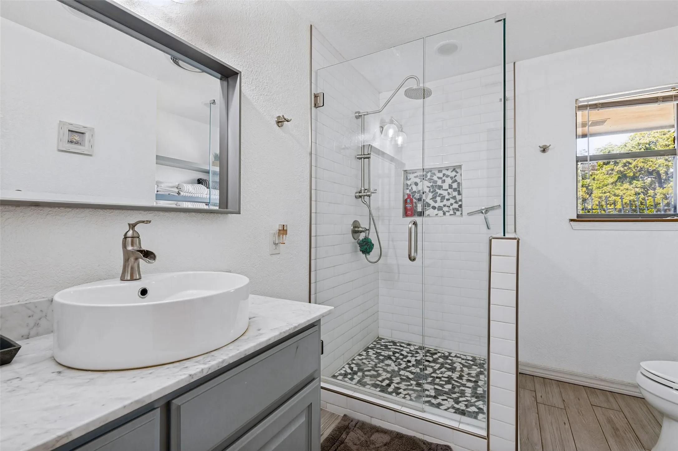 Frameless glass shower enclosure with a rainfall showerhead, tiled shower niche, and pebble-style flooring