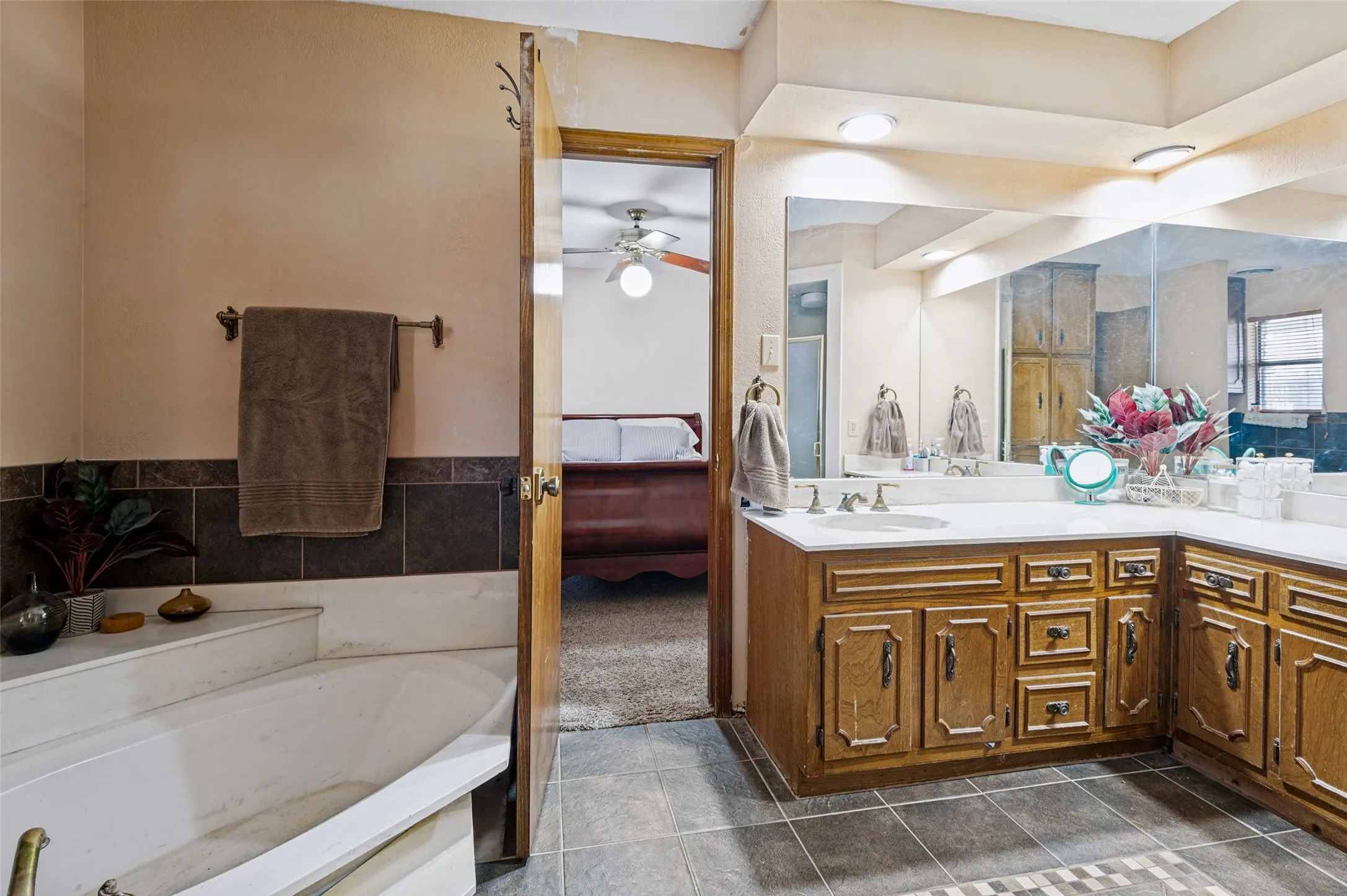Jack-and-Jill bath featuring a corner soaking tub with tiled surround, wood-finish vanity and large wall-mounted mirror.