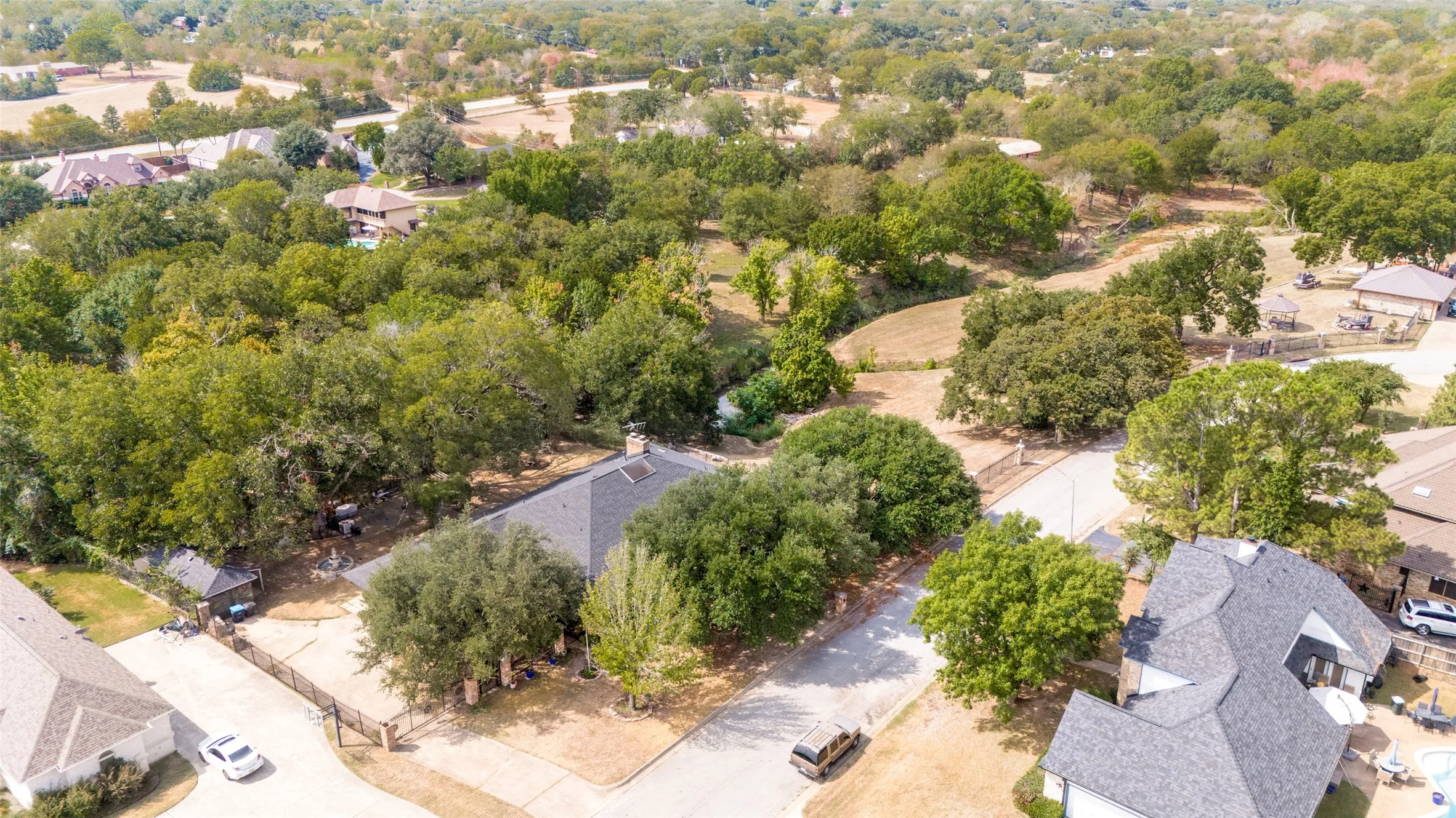 Aerial view highlighting the home's tree-filled setting and relationship to the adjoining green space and creek.