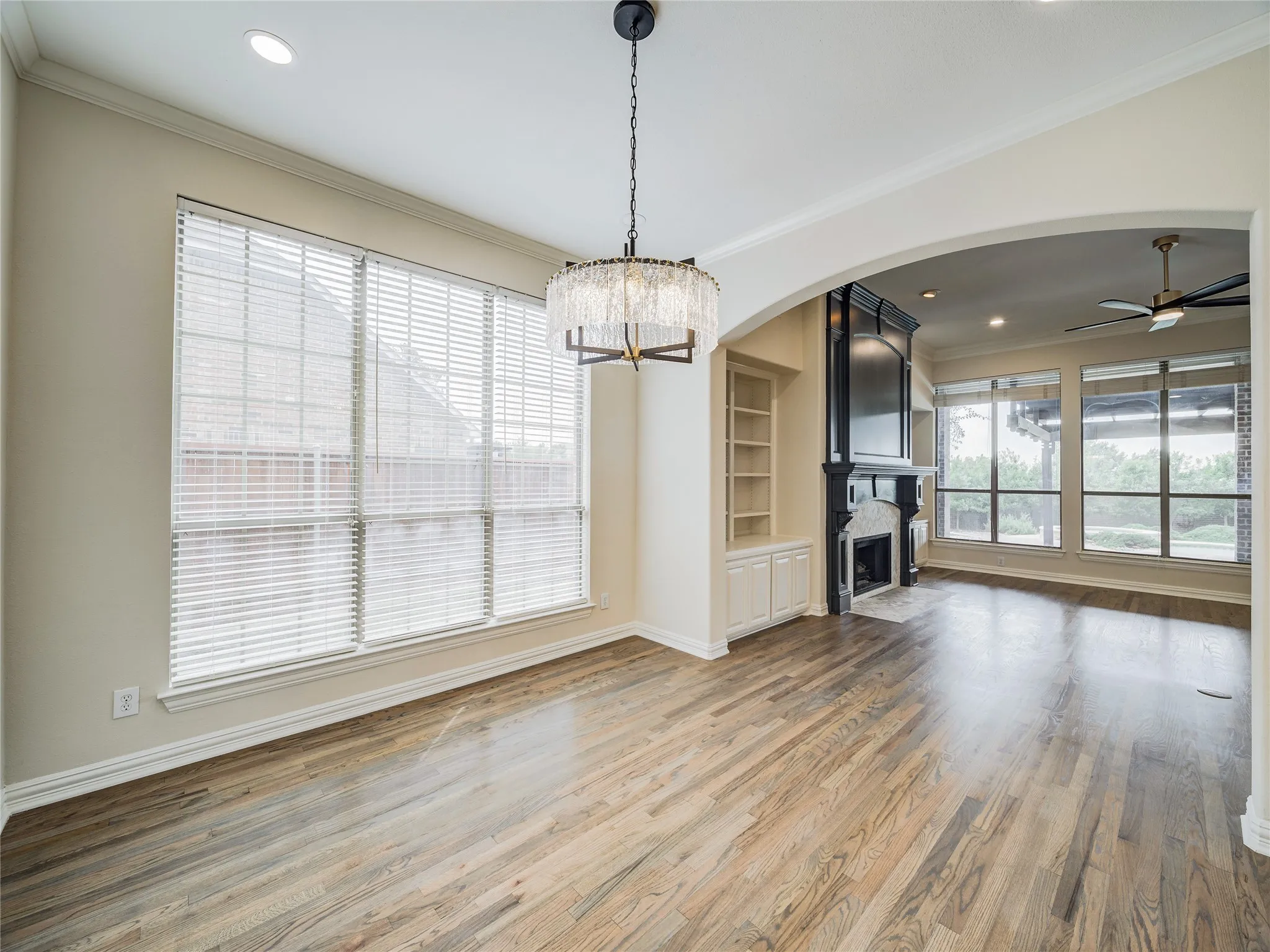 Bright, open living space featuring gleaming wood-finish flooring, expansive windows with plantation shutters flooding the room with natural light, and a contemporary pendant fixture
