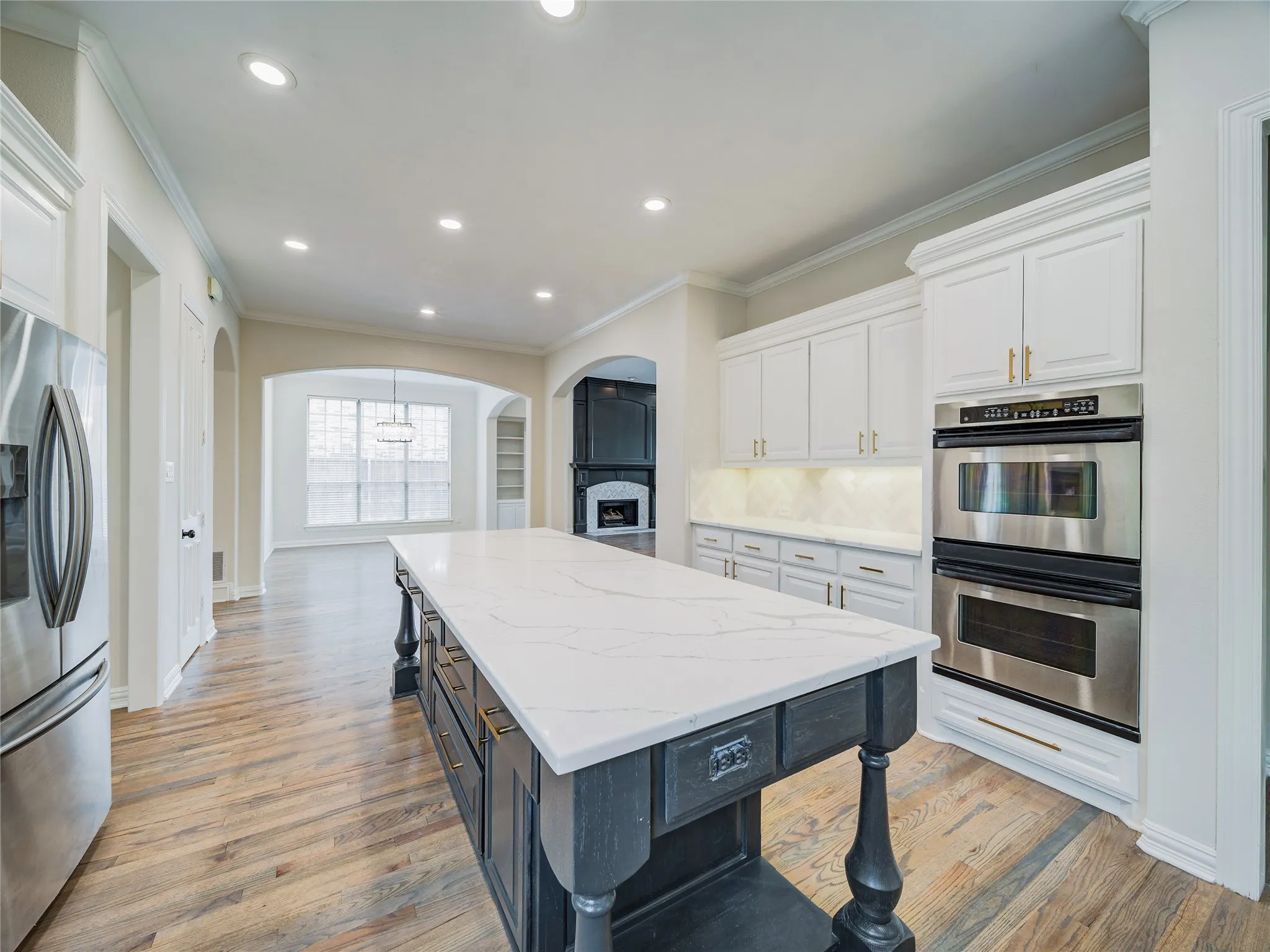 Gourmet kitchen with a large central island, white cabinetry, integrated stainless steel appliances, and wood-finish flooring