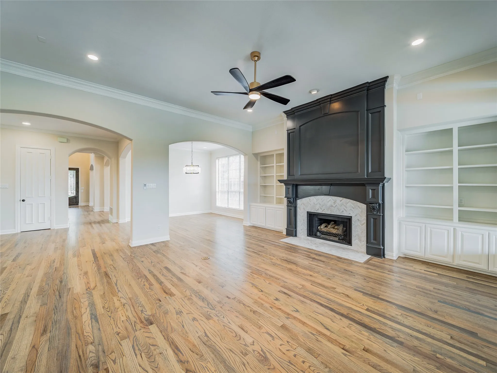 Hardwood flooring throughout, recessed lighting, arched doorways, a ceiling fan, and built-in shelving flanking a fireplace with a herringbone tile surround