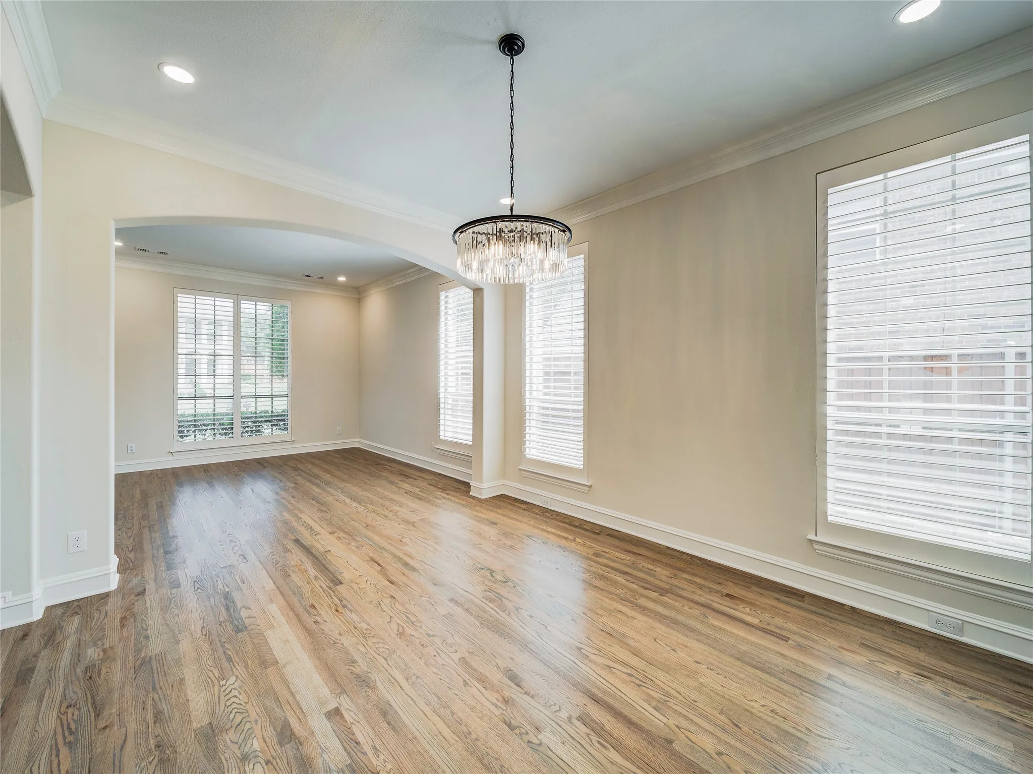 Hardwood flooring, recessed lighting, crown molding, arched entryway, and multiple windows with plantation shutters