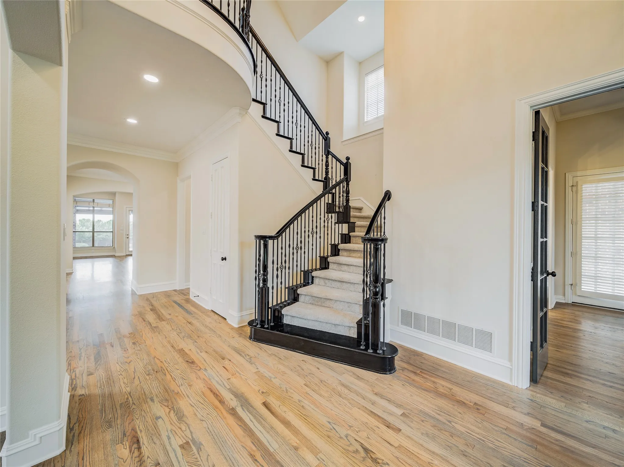Grand entry featuring a curved staircase with wrought iron balusters and carpeted treads, wood-finish flooring, recessed lighting, and arched doorways