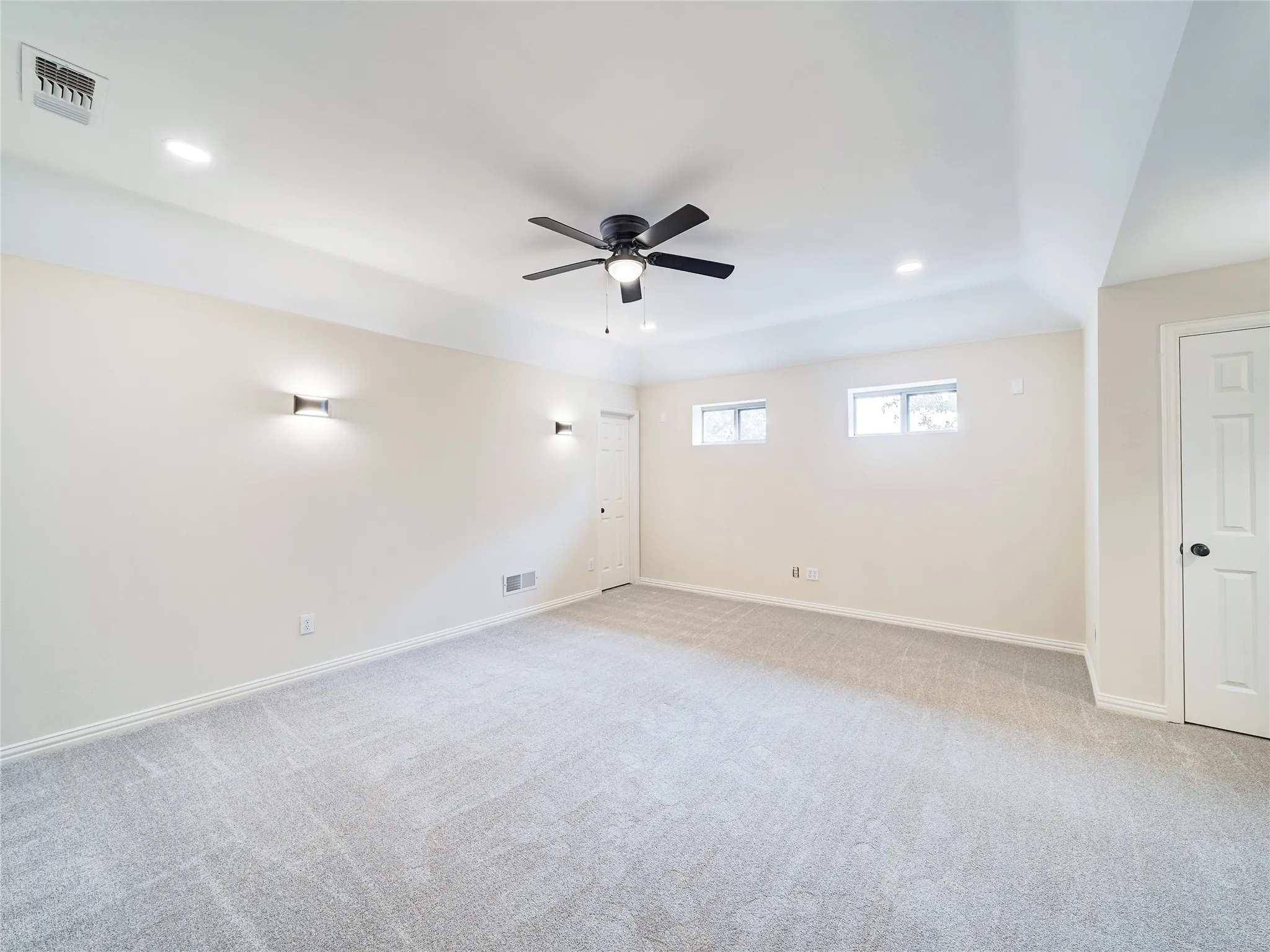 Recessed lighting, wall-mounted sconces, ceiling fan with integrated lighting, two windows, and light-toned carpeting