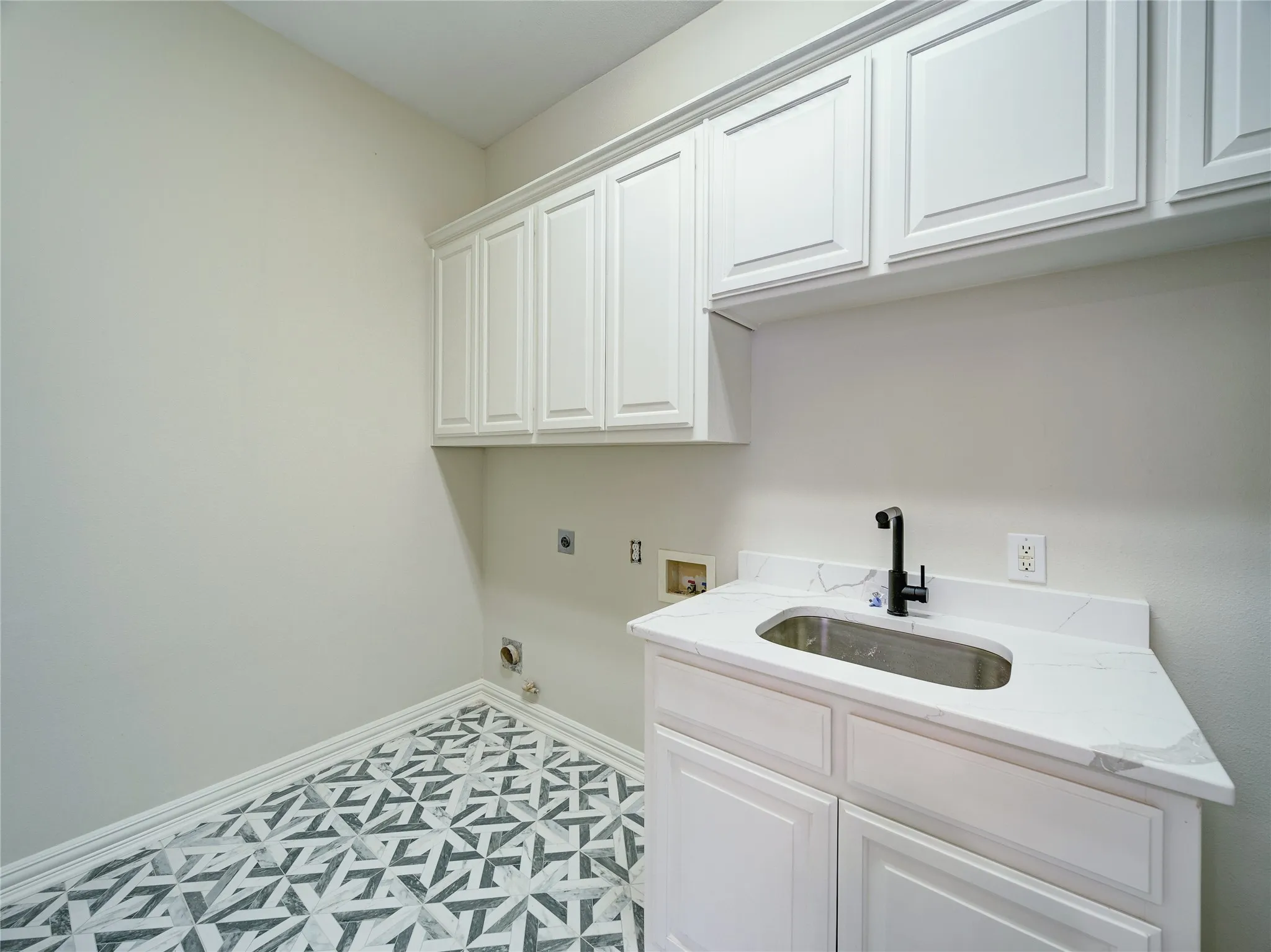 White shaker cabinetry, patterned floor tiling, white stone-finish countertop, undermount stainless steel sink, and matte black faucet