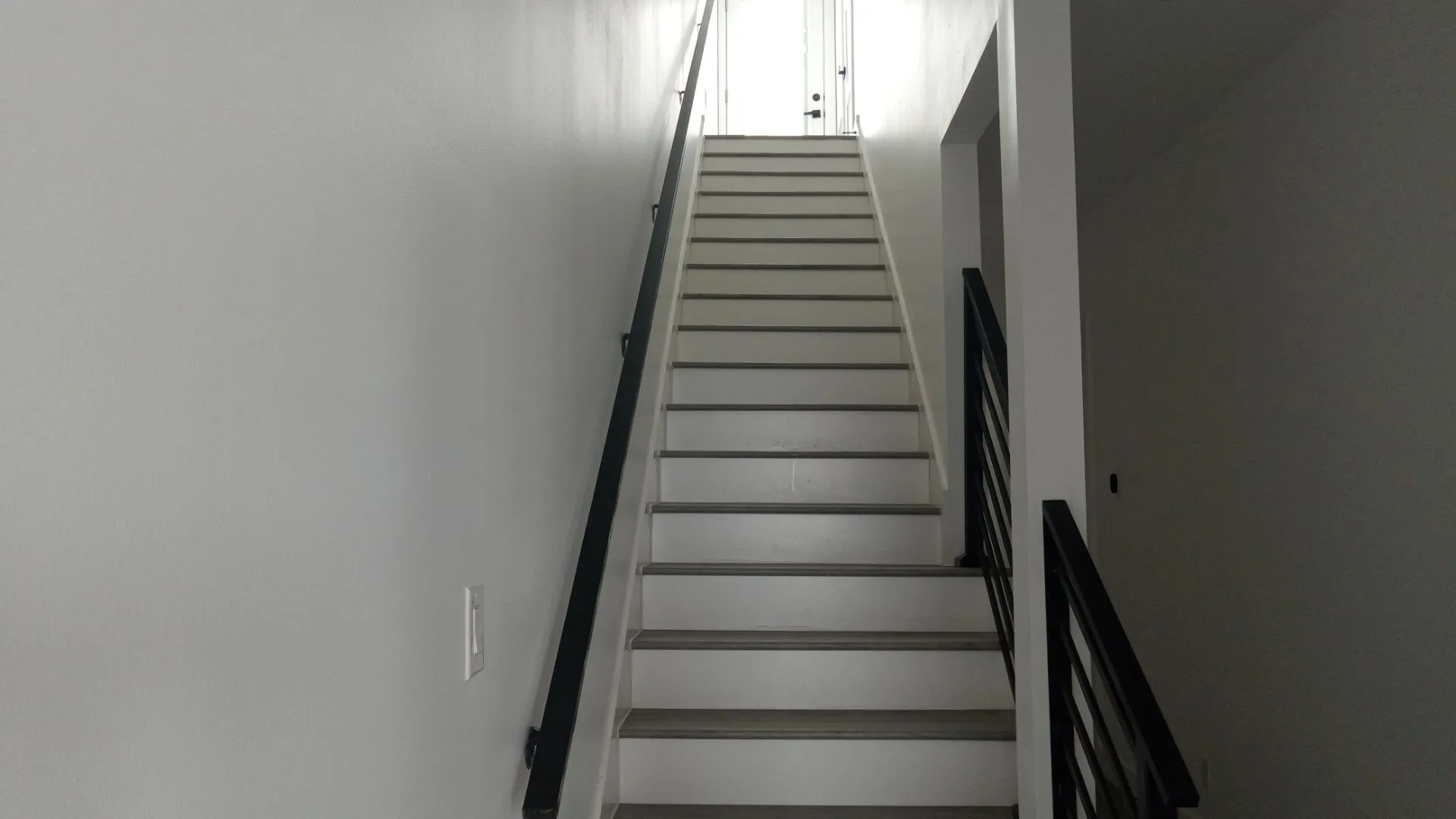 Modern staircase featuring white risers and gray treads, accented by contemporary black railings and handrails