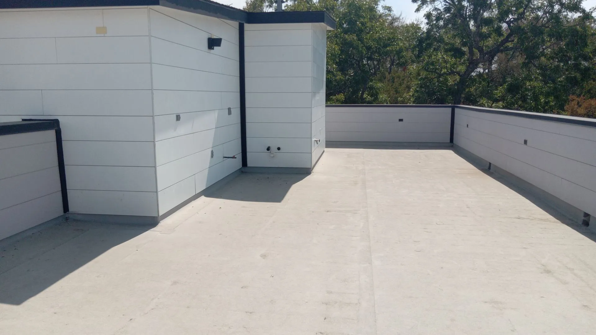 Expansive rooftop deck with a concrete surface, white panel siding, and a dark cap railing