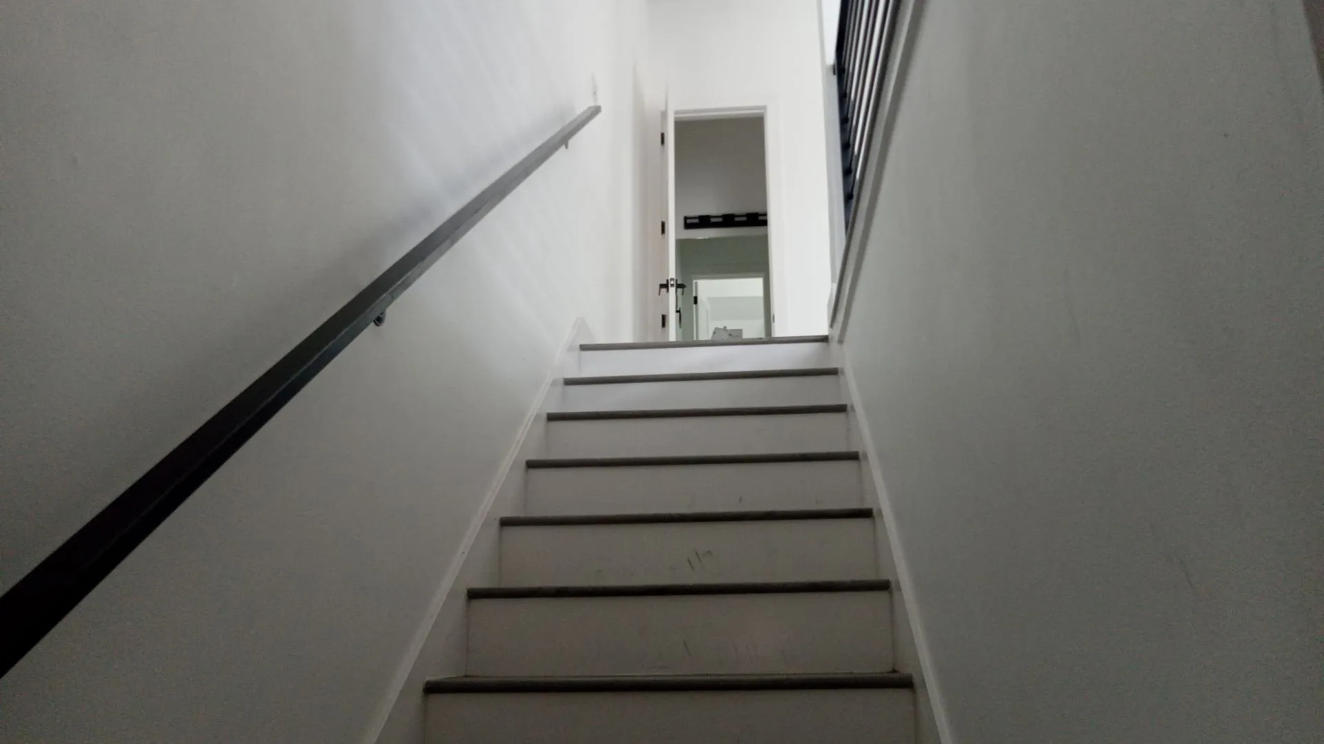 Staircase with solid treads and risers, featuring a dark wall-mounted handrail