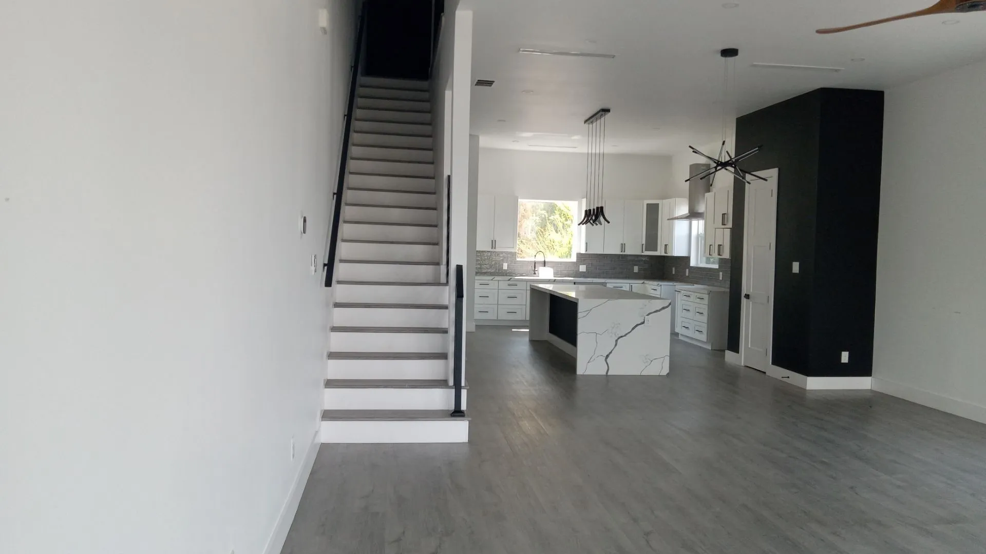 Open-concept living space with wood-finish flooring, a contemporary kitchen featuring a waterfall island, white cabinetry, and a subway tile backsplash