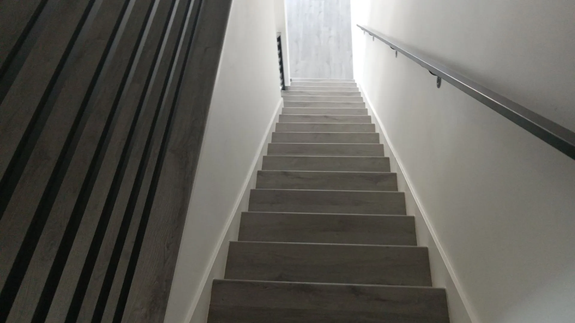 Staircase featuring wood-finish treads, a metal handrail, and a decorative wood-slat wall panel