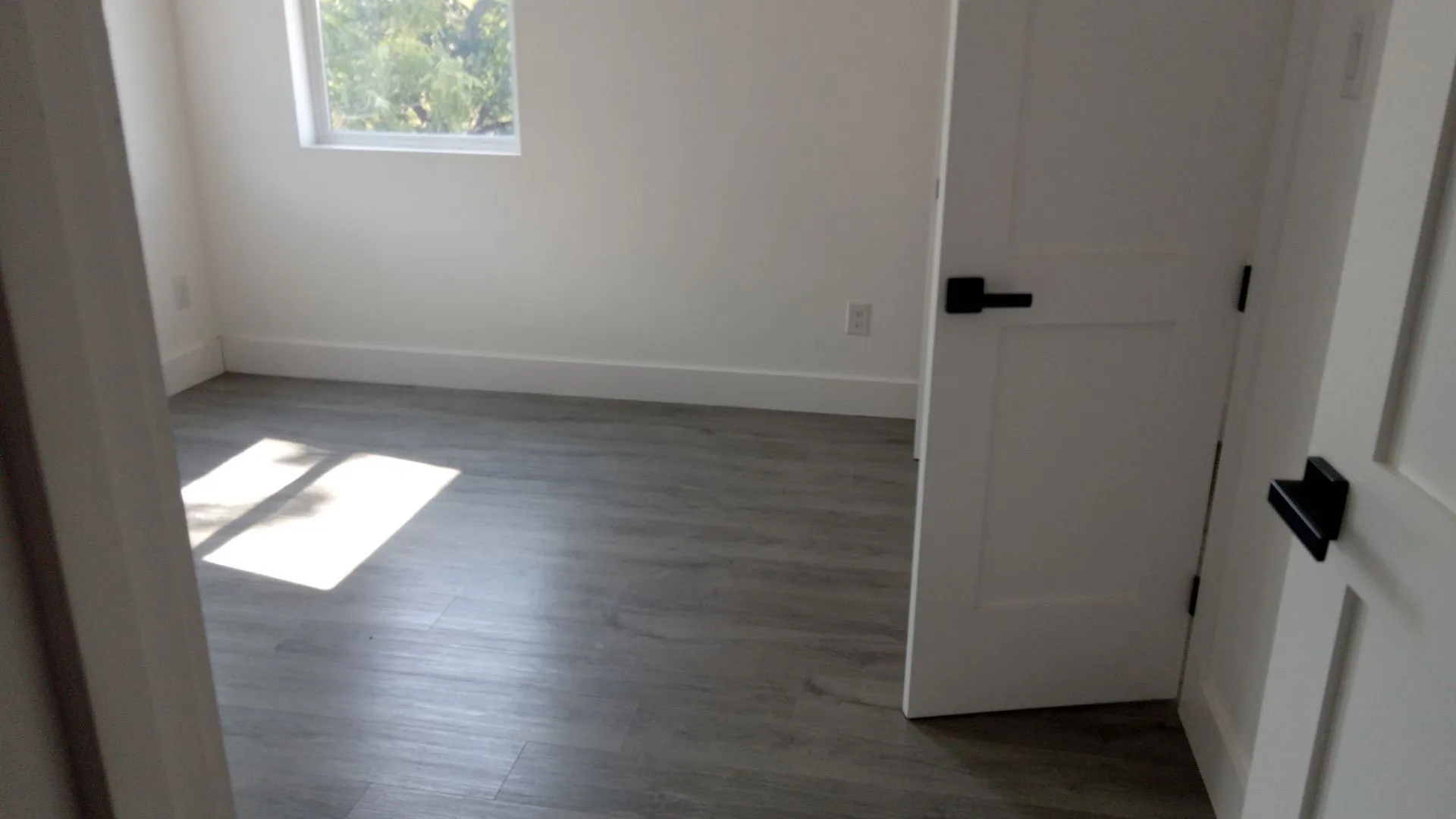 Neutral gray wood-finish flooring, white baseboards, and a single pane window