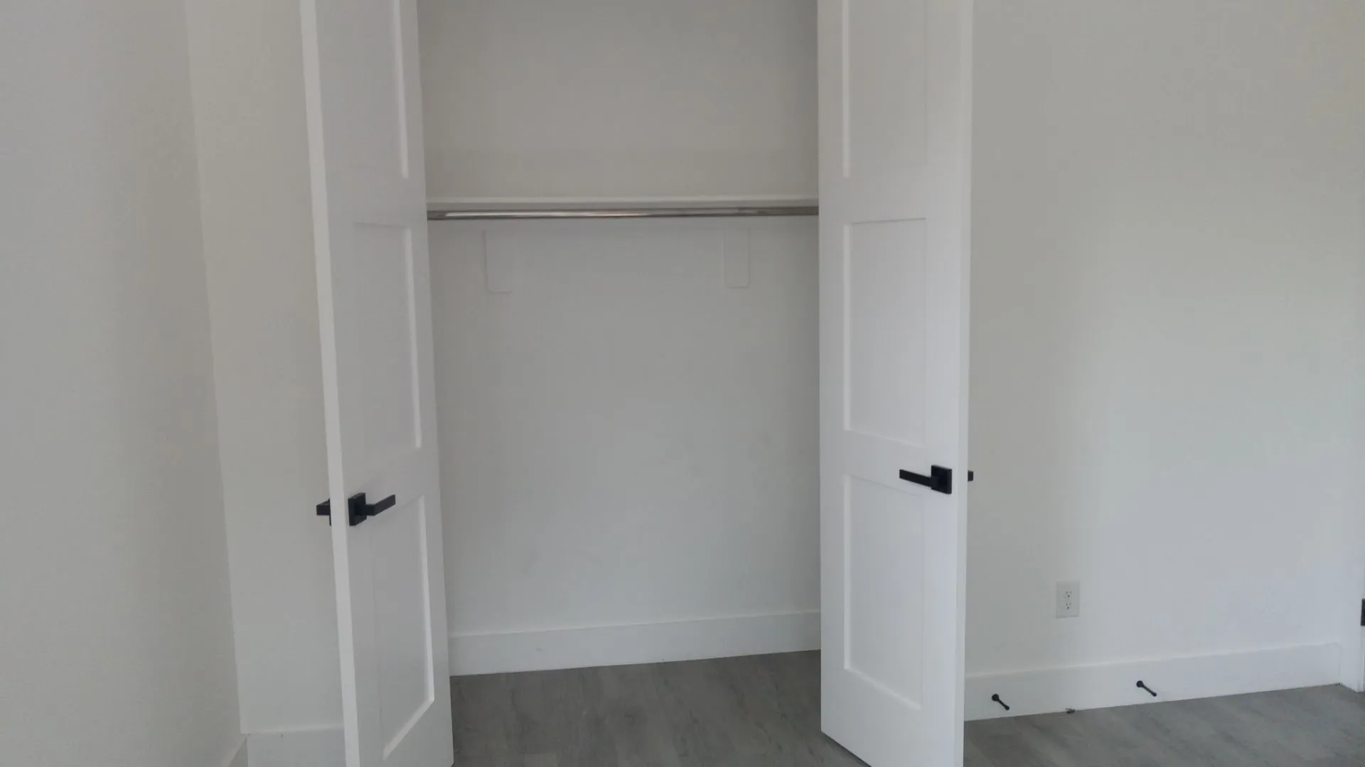 Built-in closet with panel doors and a metal hanging rod, featuring matte black hardware and wood-finish flooring
