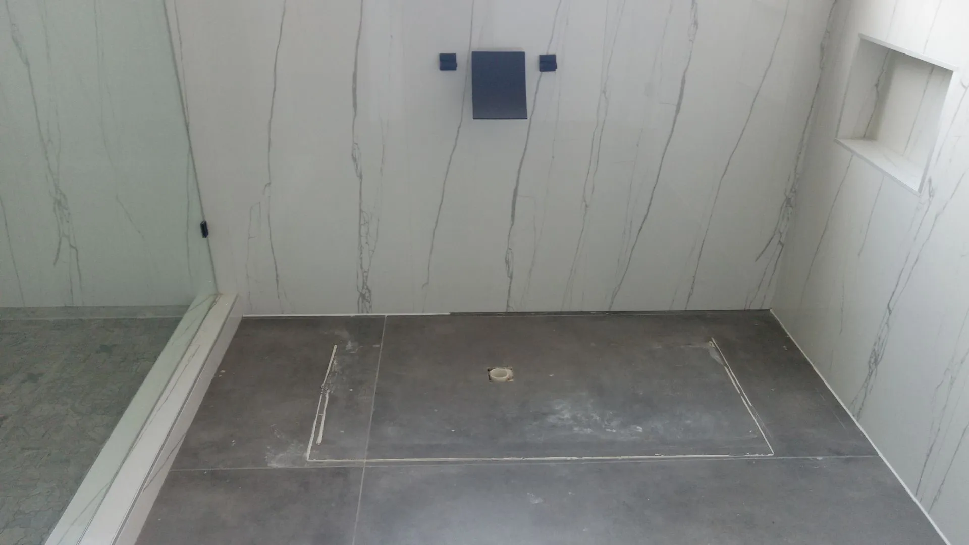 Walk-in shower with full-height white marble-look tile walls, integrated wall niche, and dark large-format floor tile