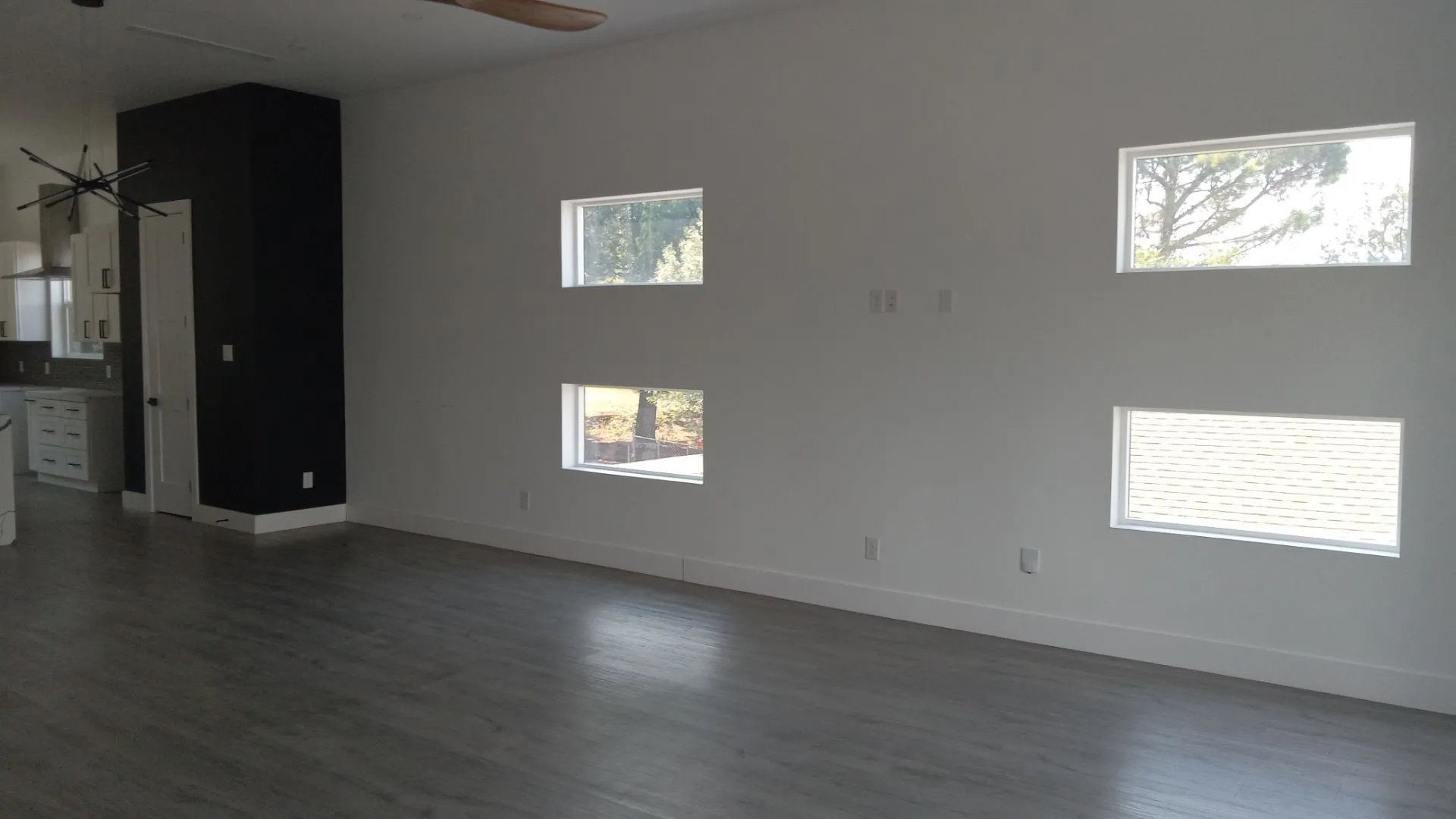 Open-concept living space with multiple rectangular windows, wood-finish flooring, and a contemporary ceiling fan
