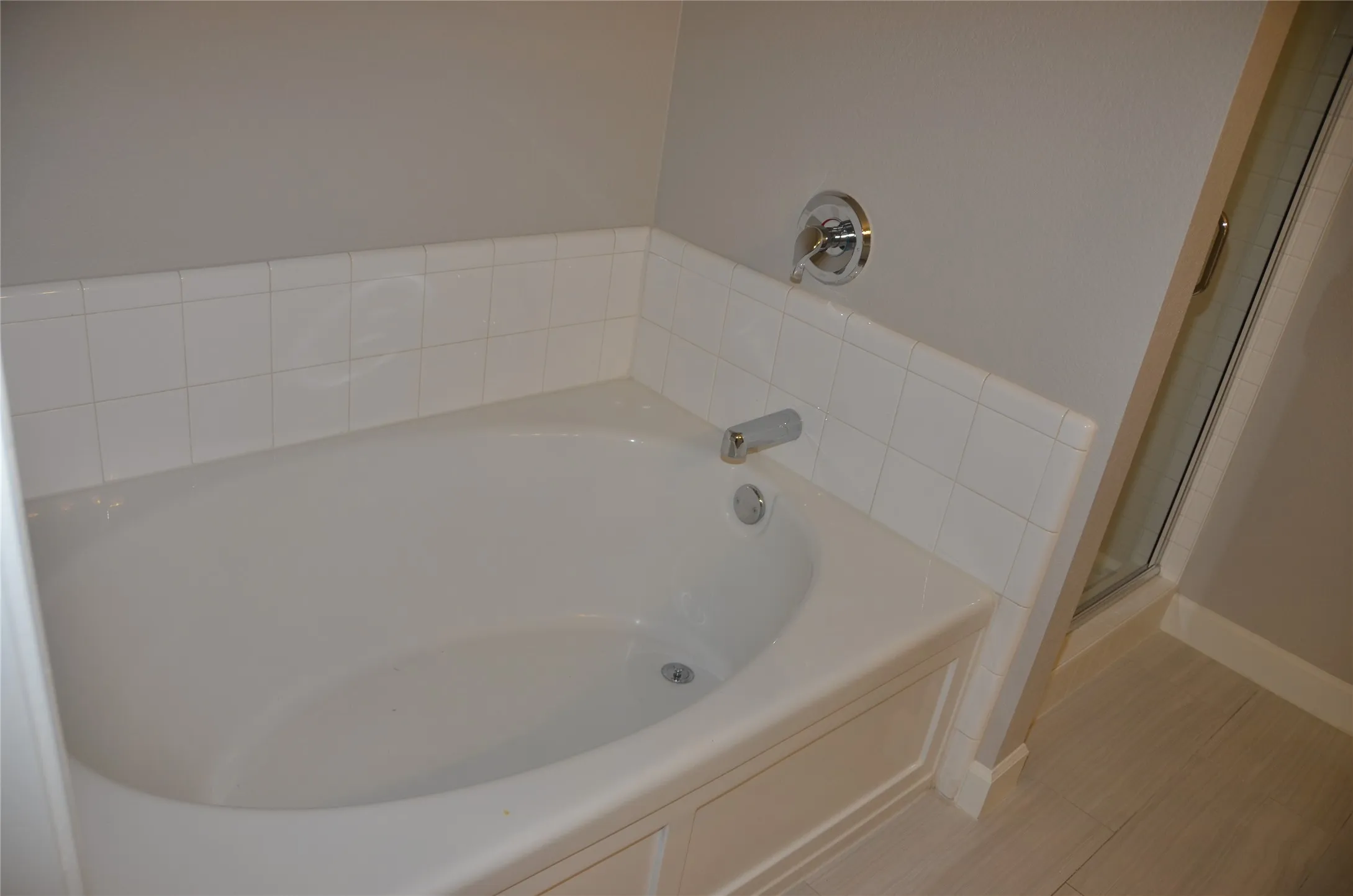 Built-in soaking tub with chrome fixtures, white tile surround, and a glass-enclosed shower