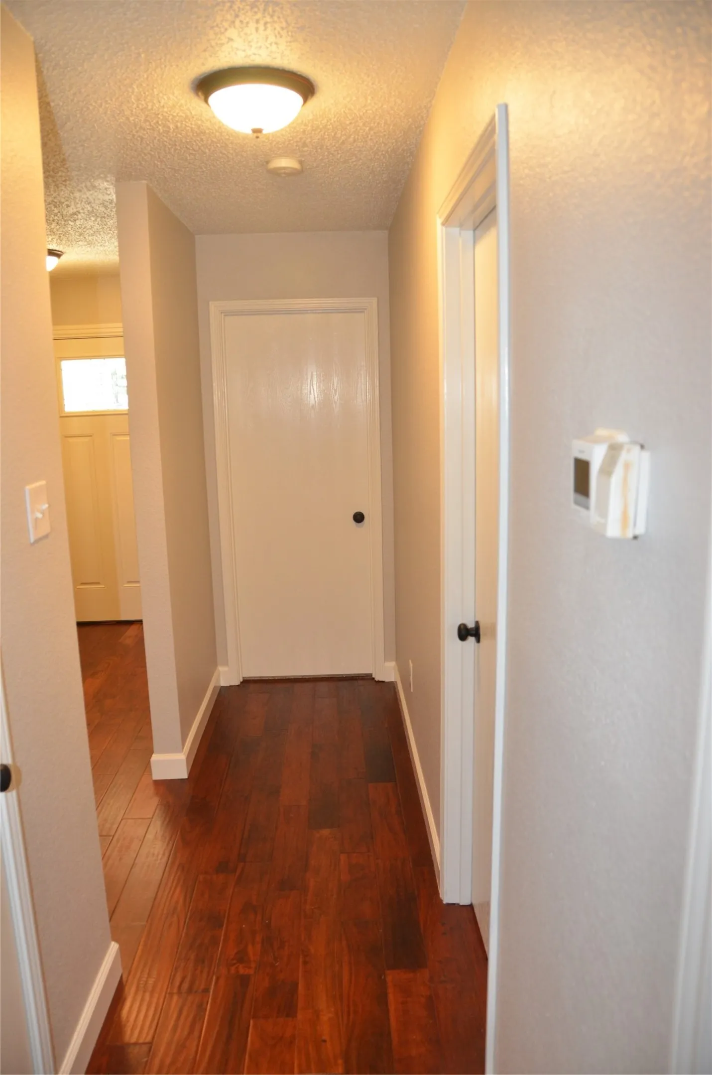 Hallway featuring rich wood-finish flooring, white doors with black hardware, and a ceiling-mounted light fixture