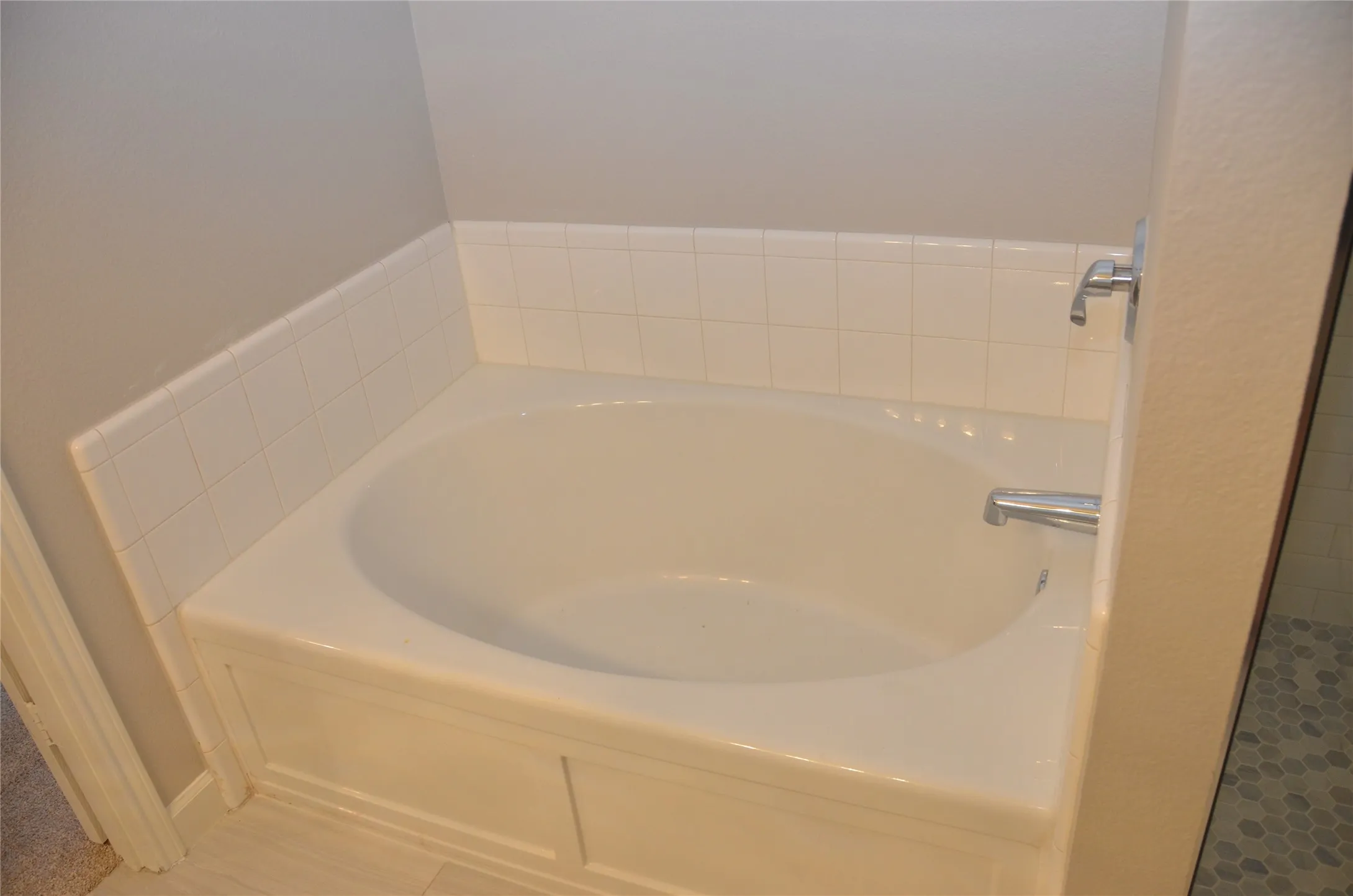 White drop-in garden tub with chrome fixtures, surrounded by white subway tile wainscoting and light gray walls