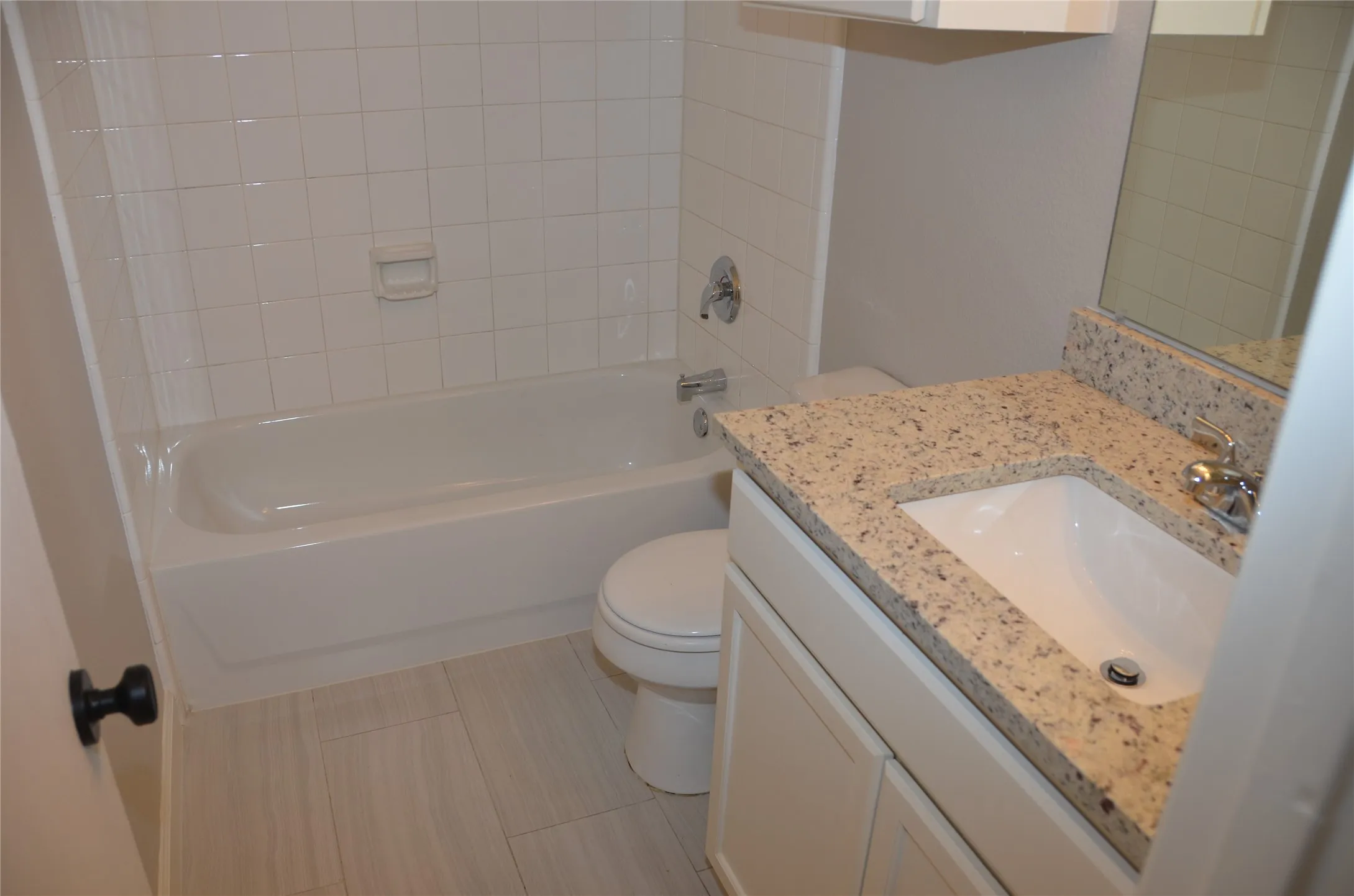 Updated full bathroom featuring a ceramic tile surround, alcove bathtub with shower combination, porcelain toilet, and granite-topped vanity with an undermount sink and single-handle faucet
