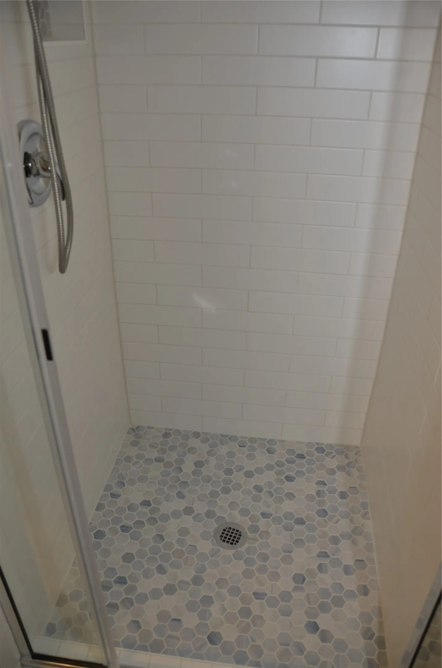 Shower enclosure featuring subway tile walls, hexagonal floor tiling, and a chrome shower fixture