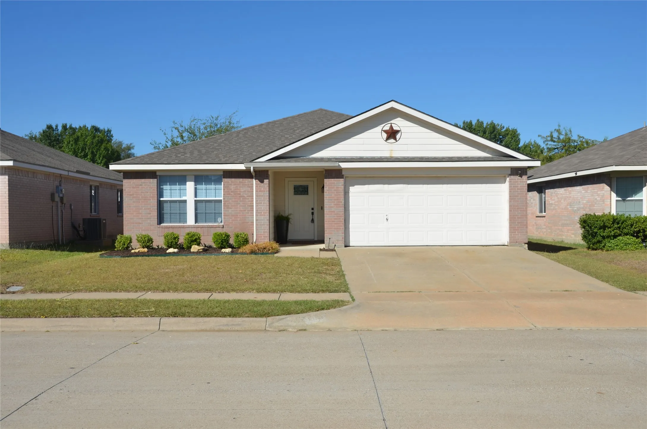Brick facade with white trim, attached garage with a concrete driveway, and a front yard with manicured landscaping