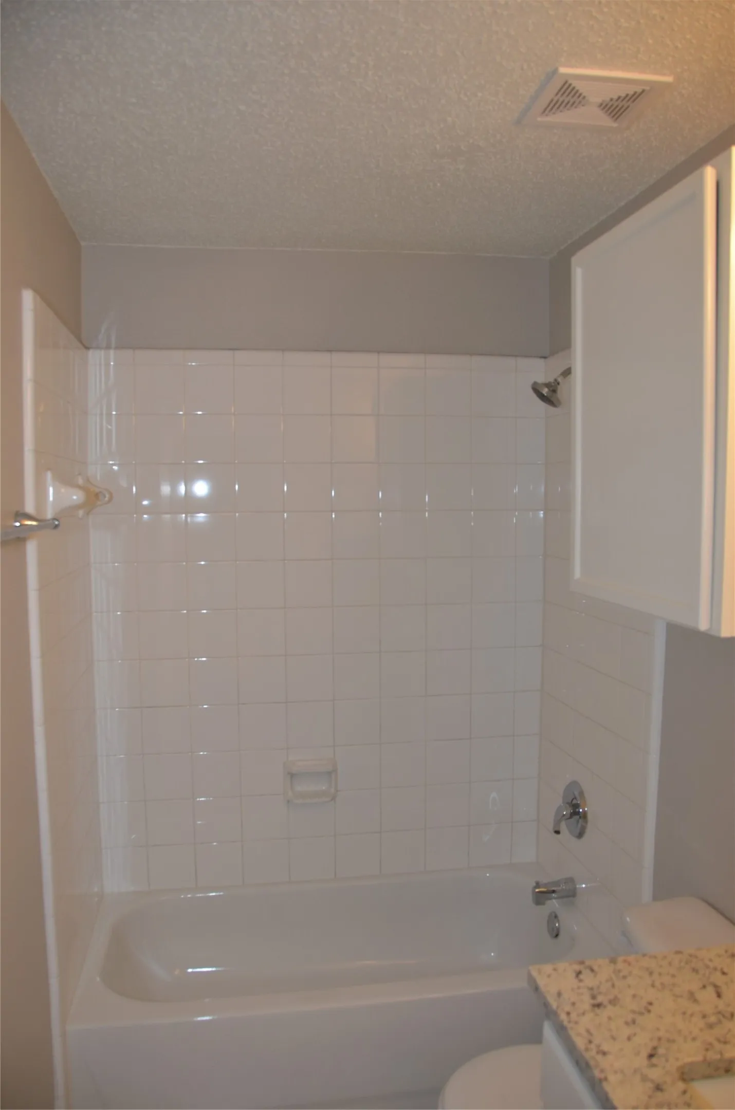White tiled shower surround, integrated bathtub, chrome fixtures, and a granite-look vanity countertop